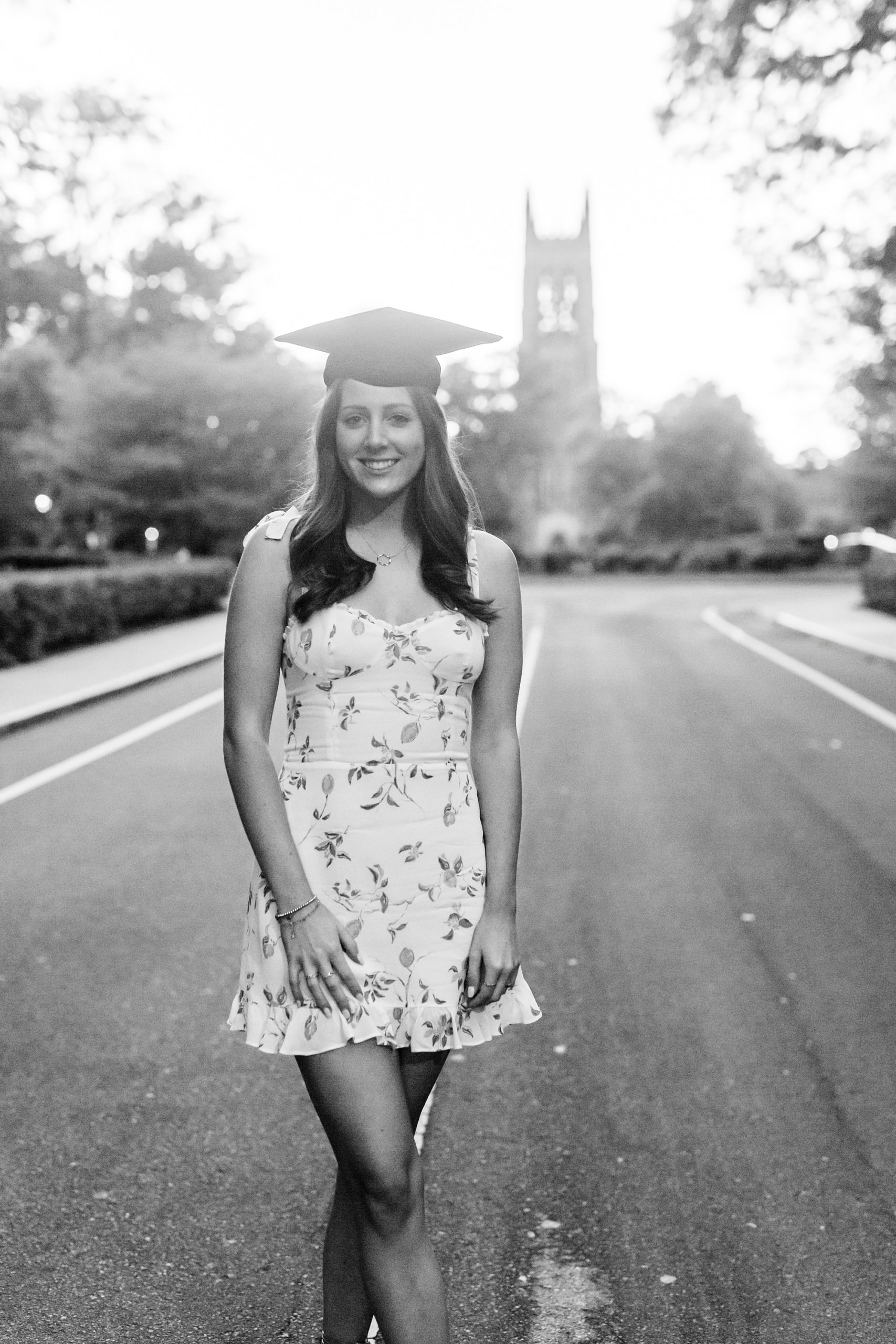 college senior in cap poses by bell tower in Duke University