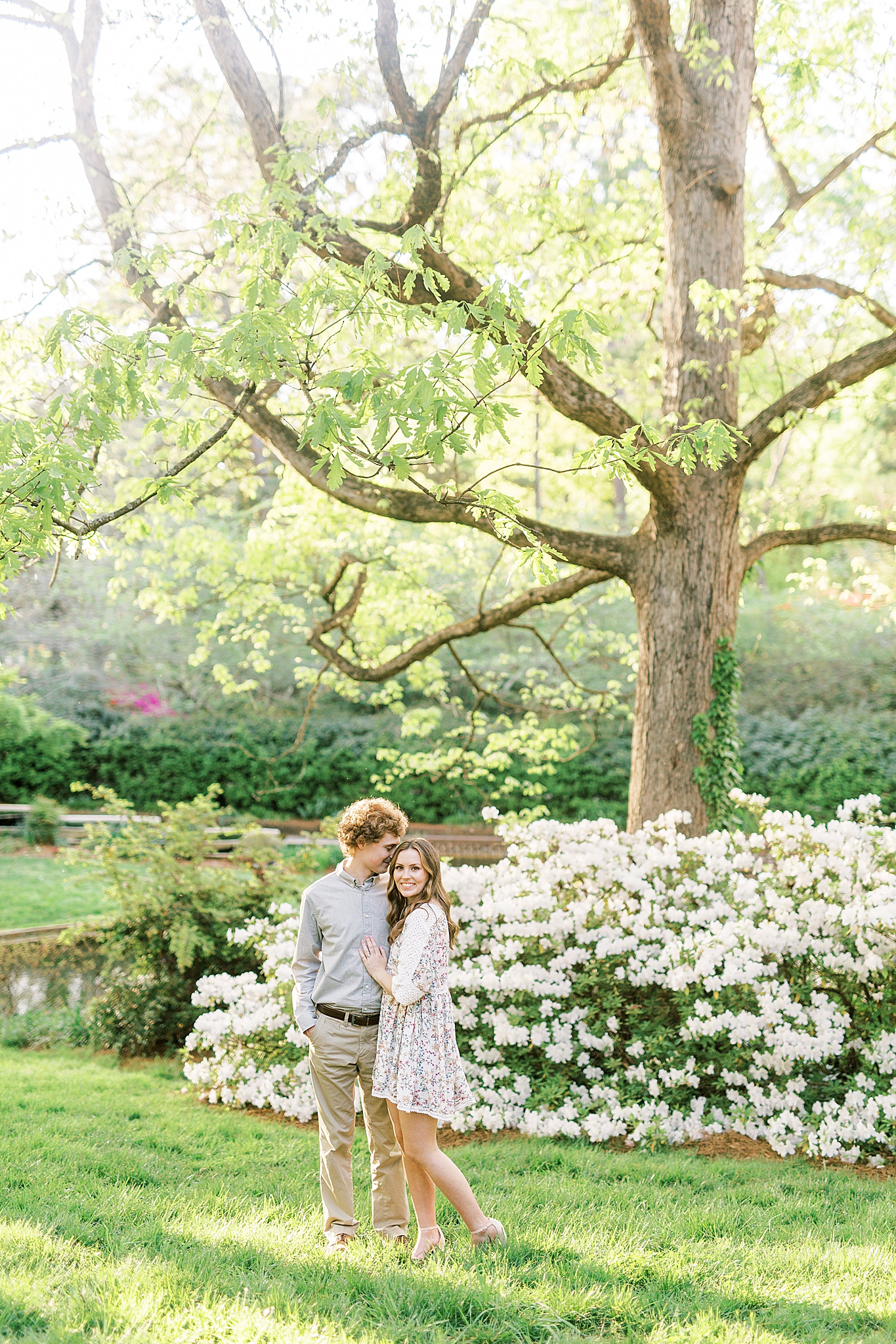 couple poses under tree by white bush in Glencairn Gardens