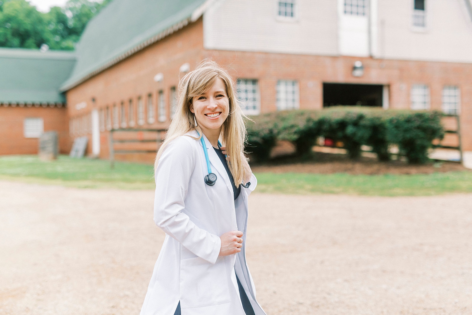 college graduate poses in white coat outside barn