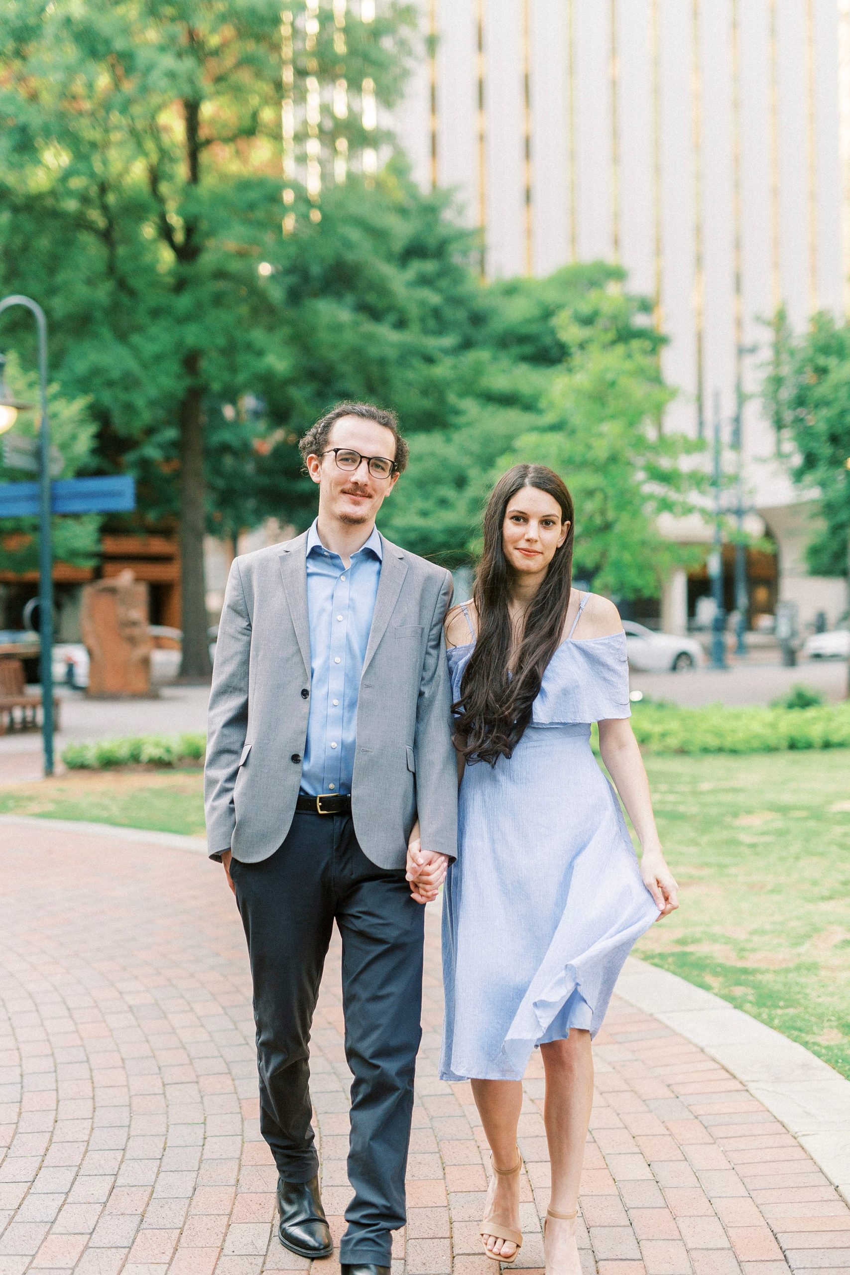 engaged copule walks through Uptown Charlotte park