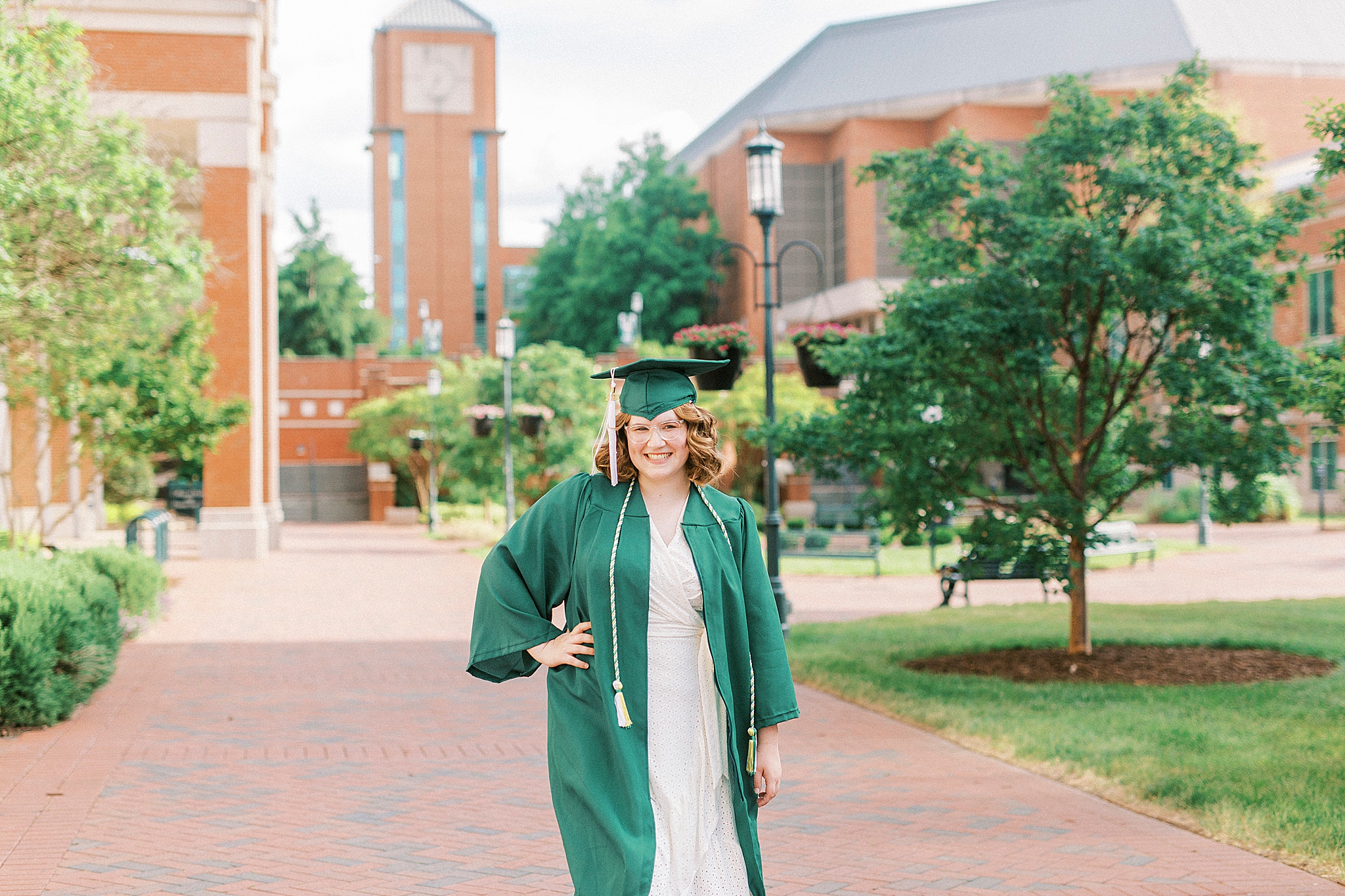 senior in green robe poses on UNCC campus