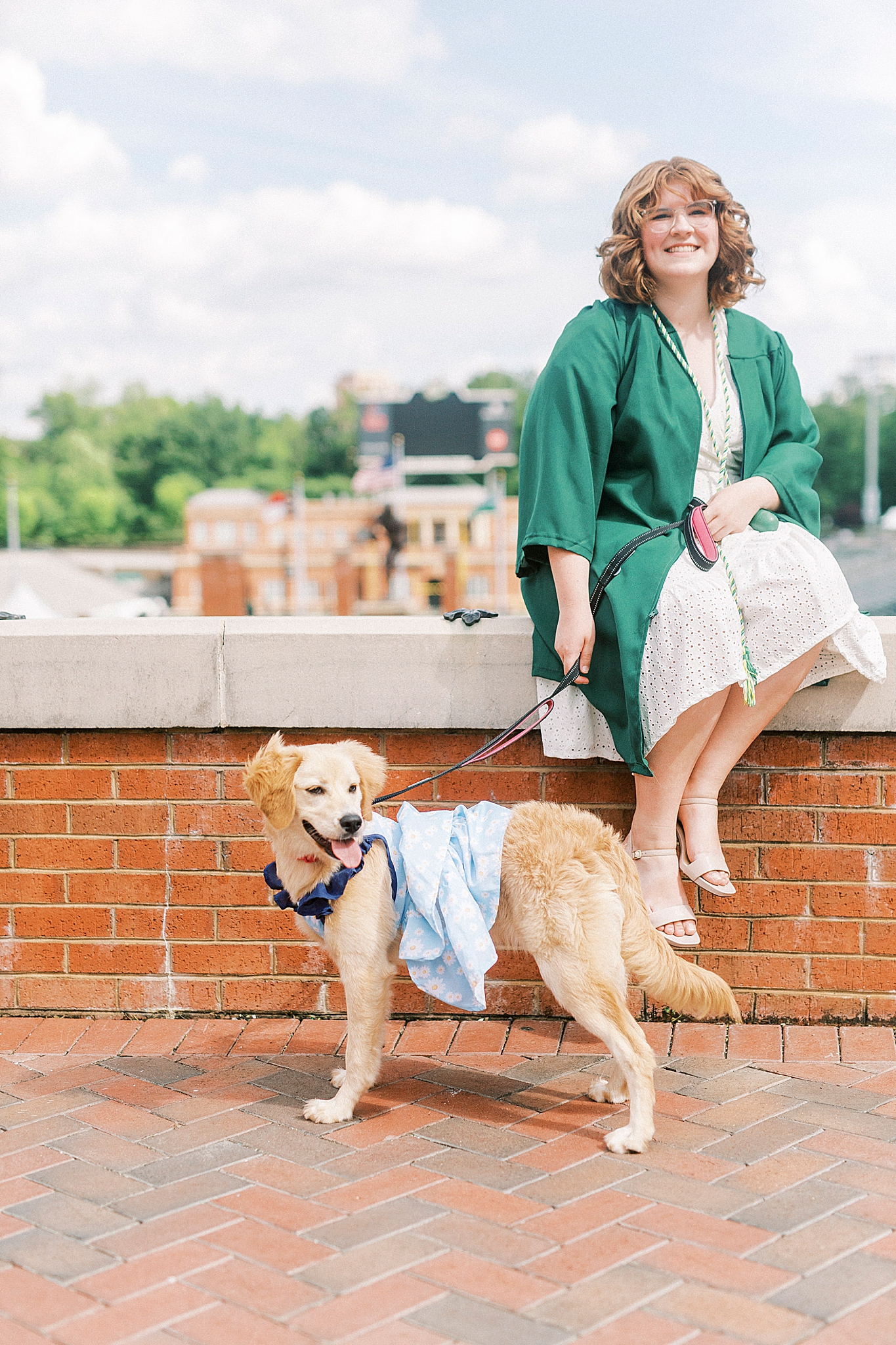 graduate sits on brick wall during UNCC senior pictures