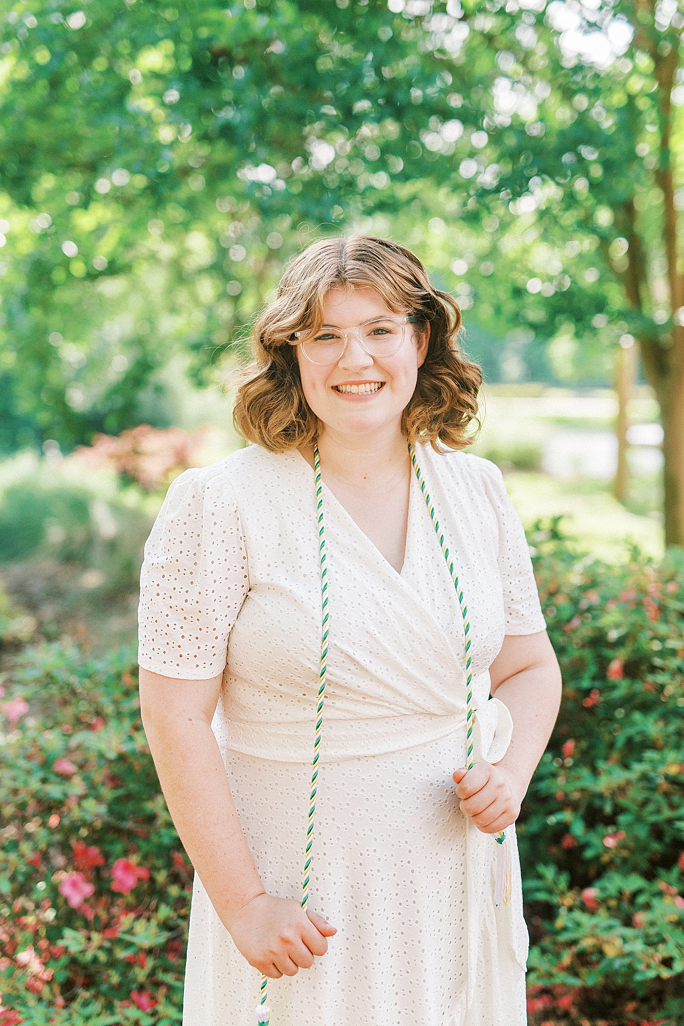 college graduate poses in white dress with cords