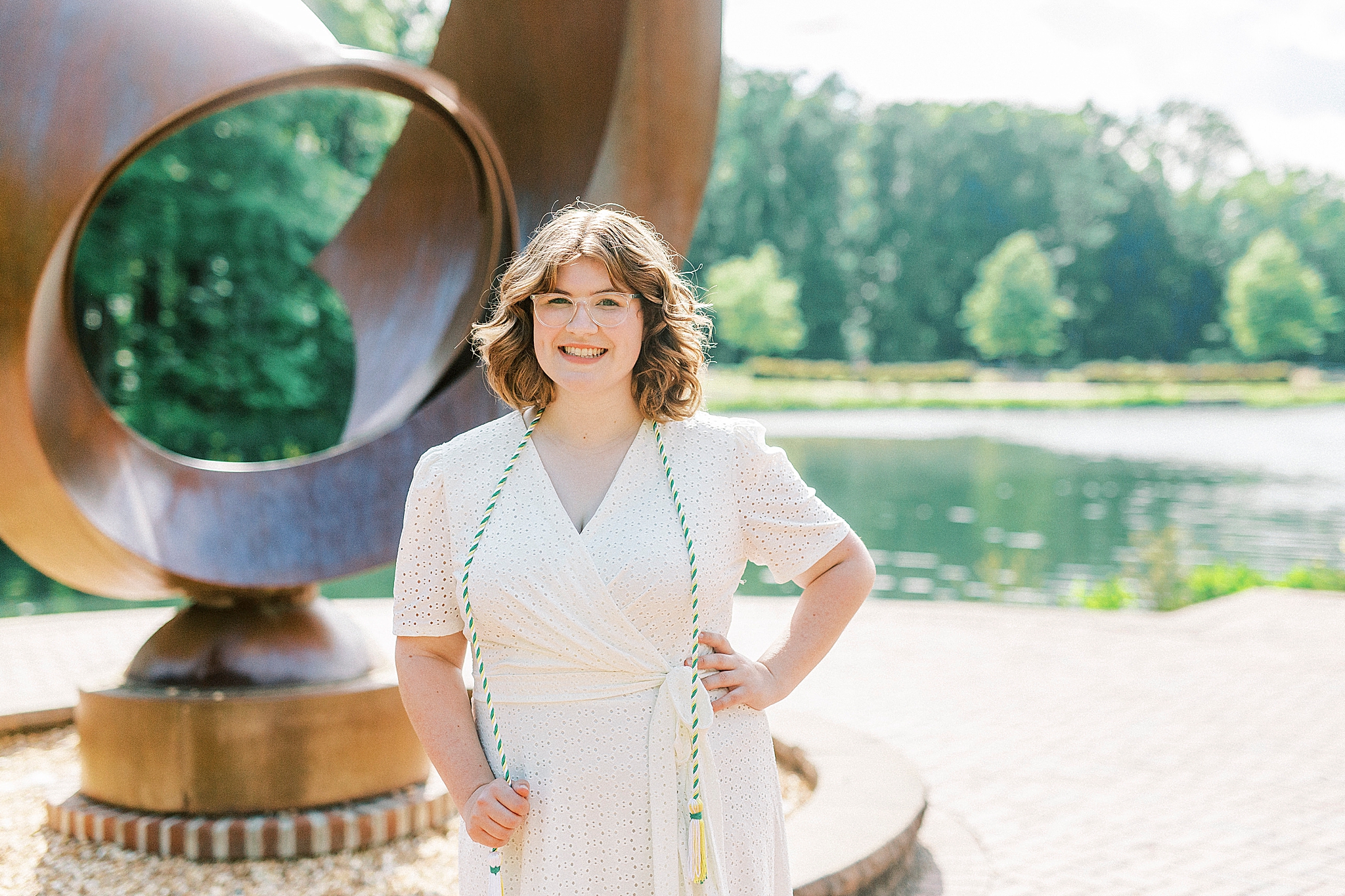 college graduate poses in white dress with green cords