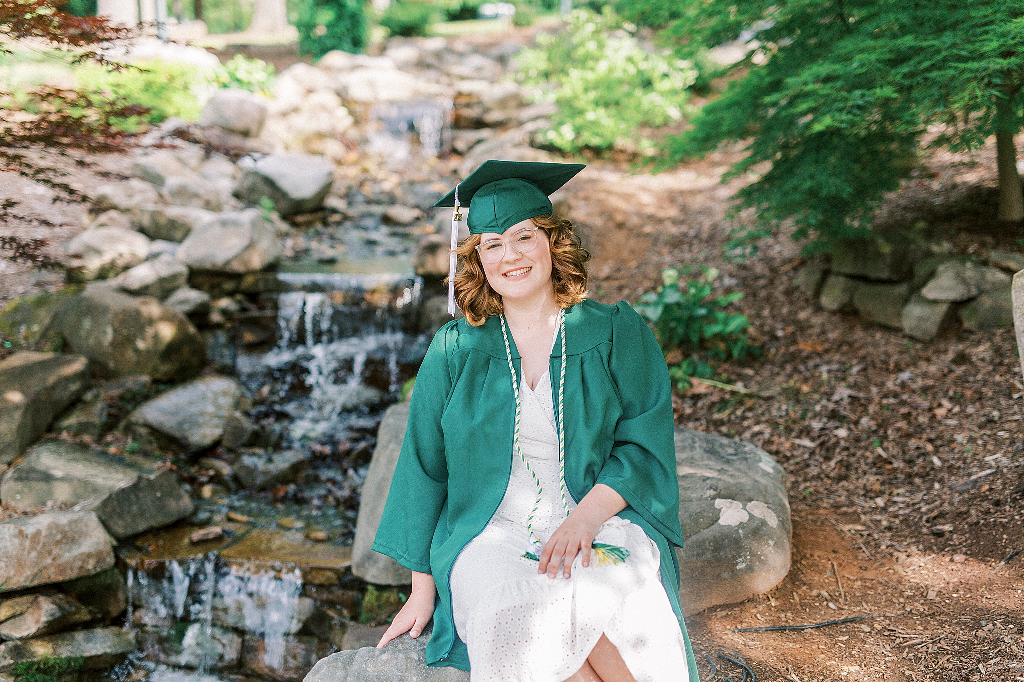 senior sits on rocks by lake at UNCC