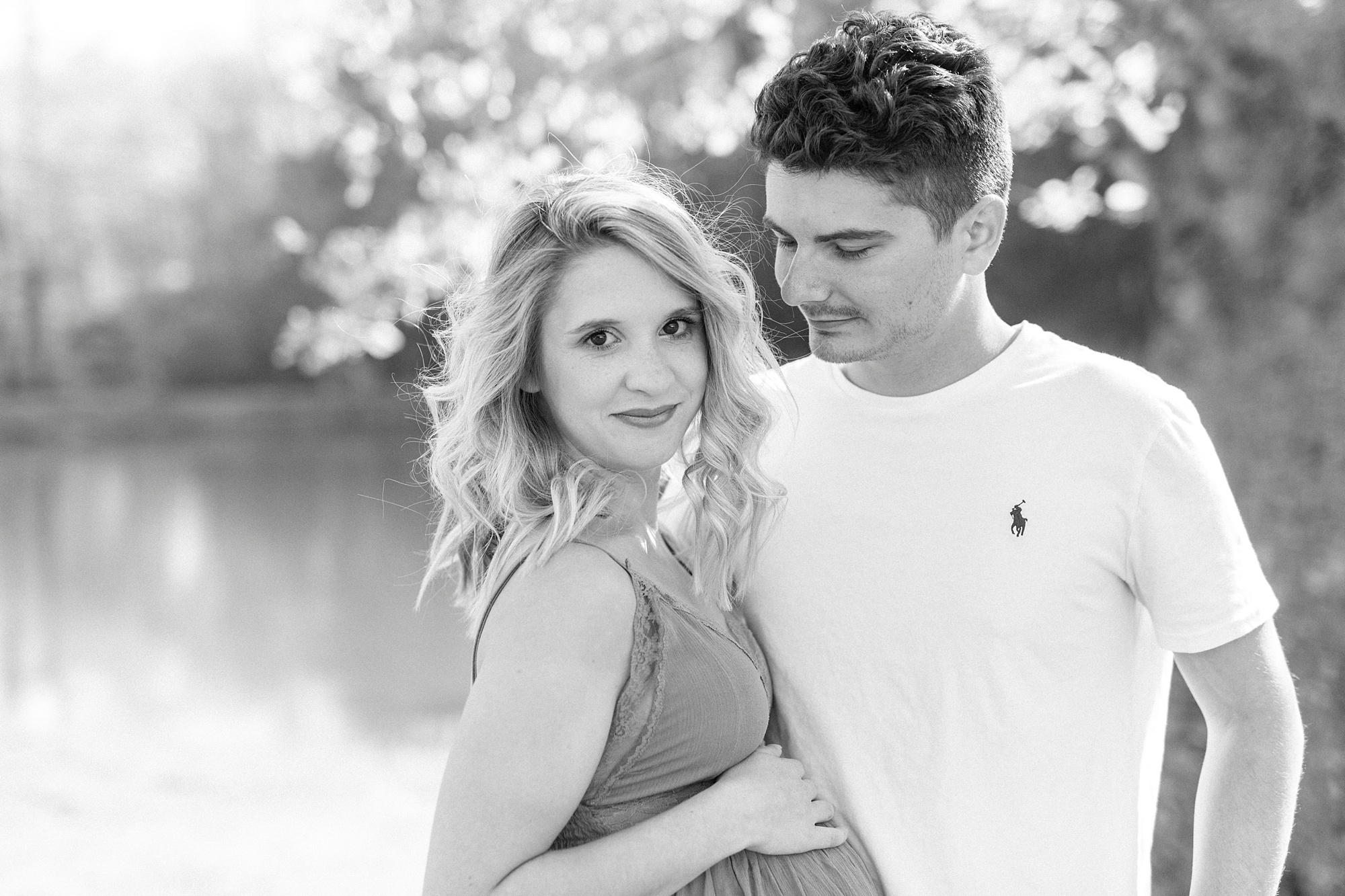 dad looks down at mothe during maternity portraits by lake