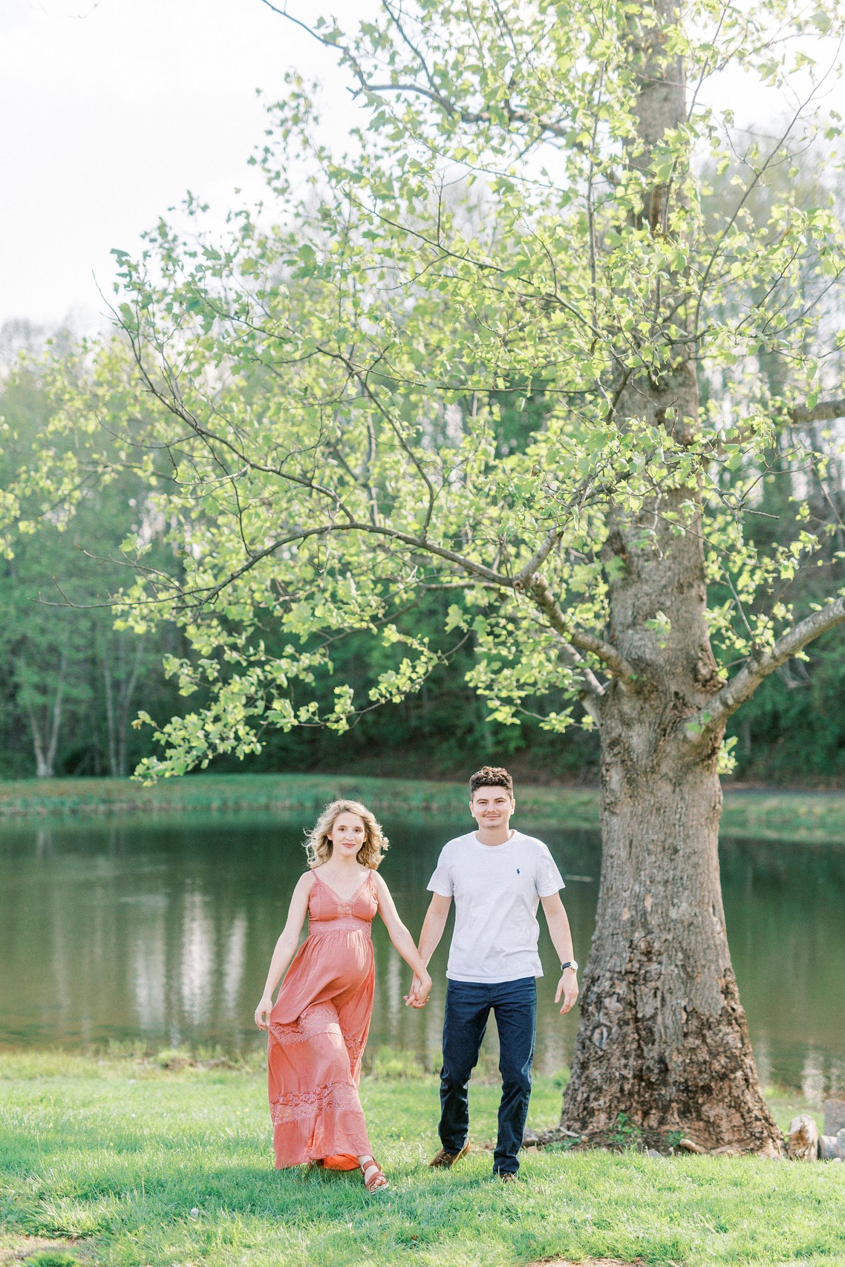 couple holds hands walking through field during maternity photos