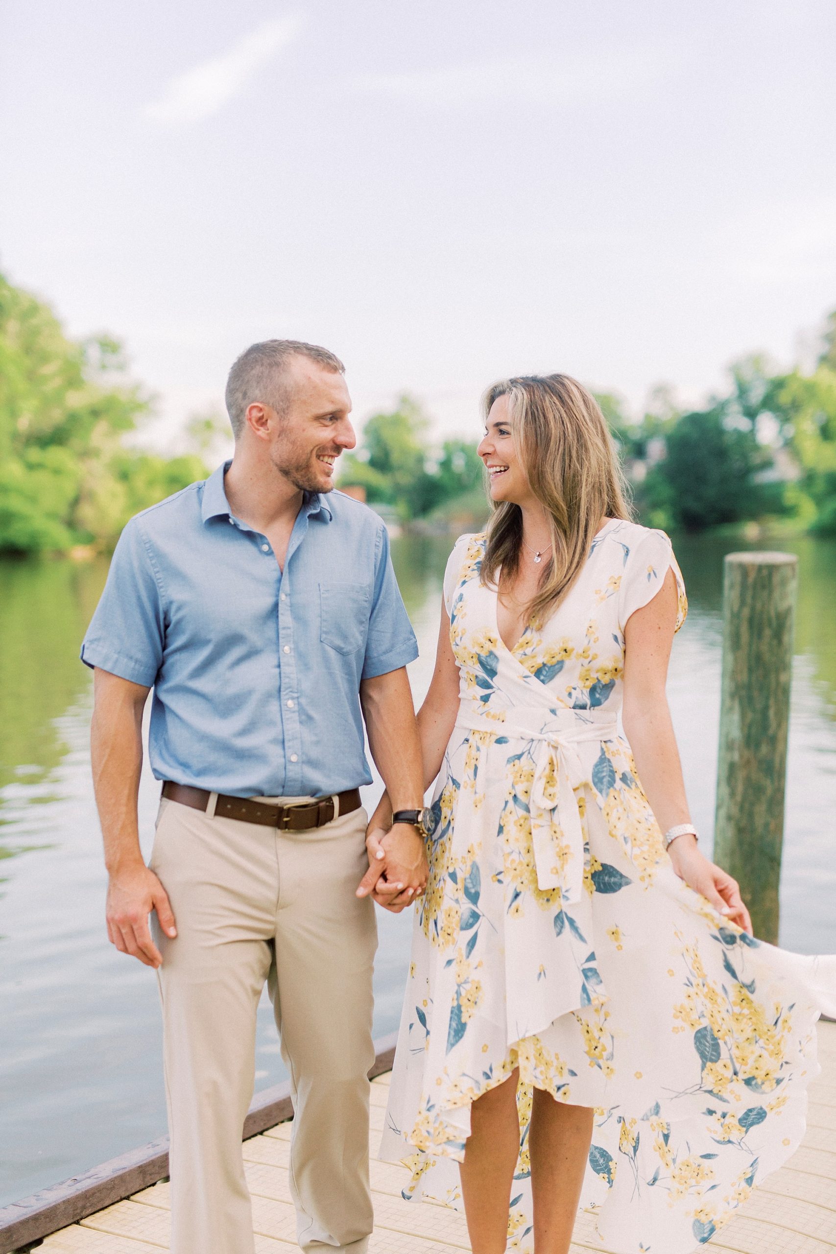 engaged couple holds hands walking on wooden pier in Kevin Loftin Park