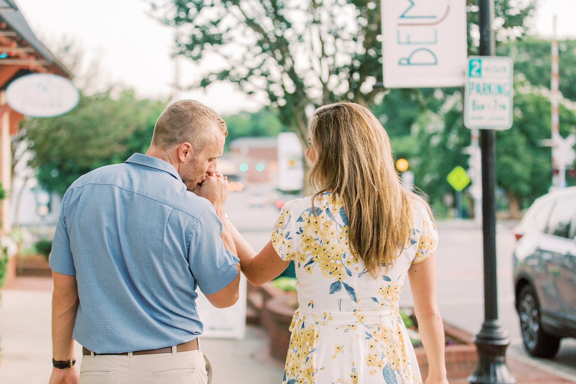 groom kisses bride's hand while they walk down sidewalk