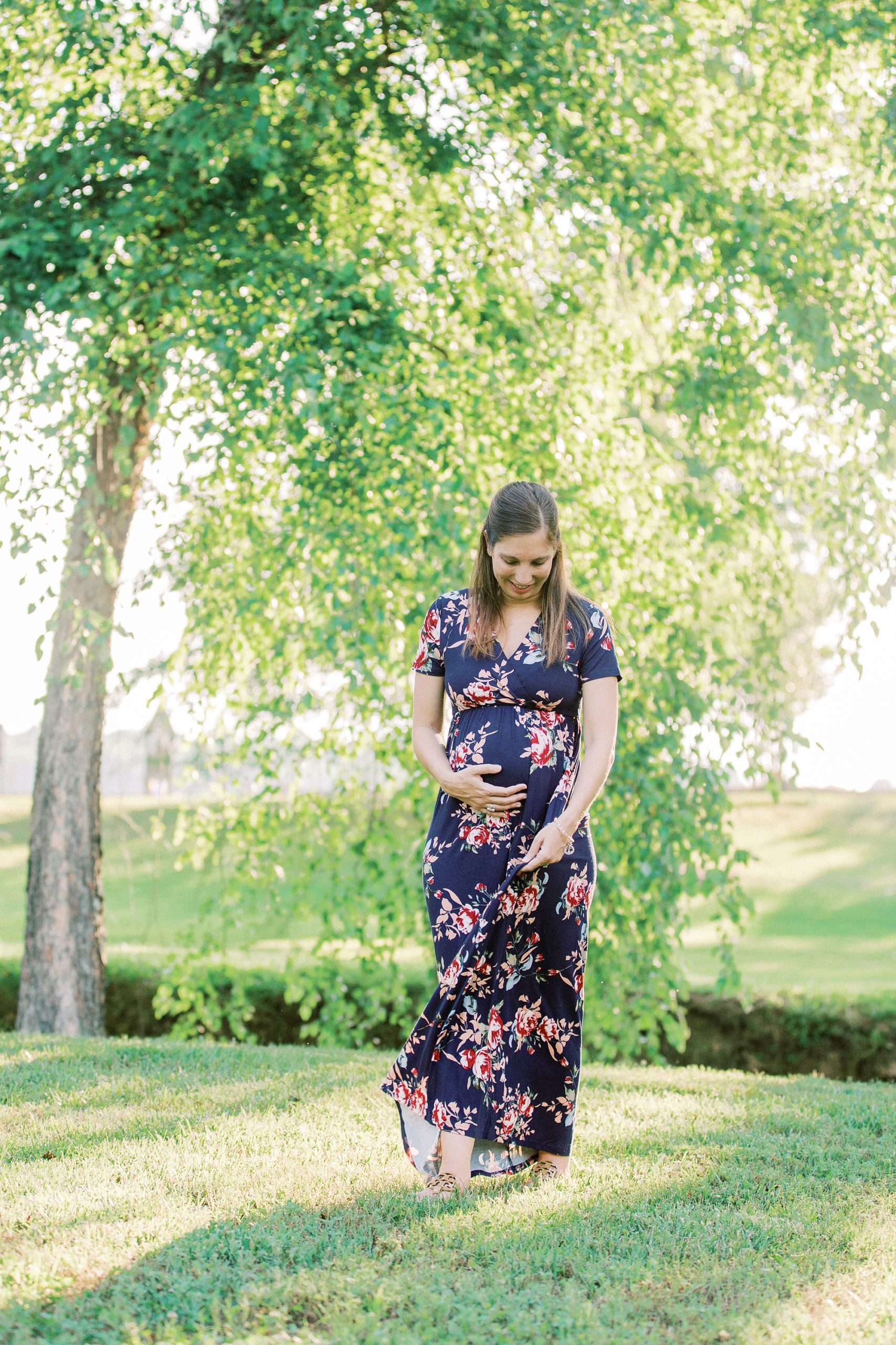 woman in blue dress walks through Rankin Lake Park during maternity photos