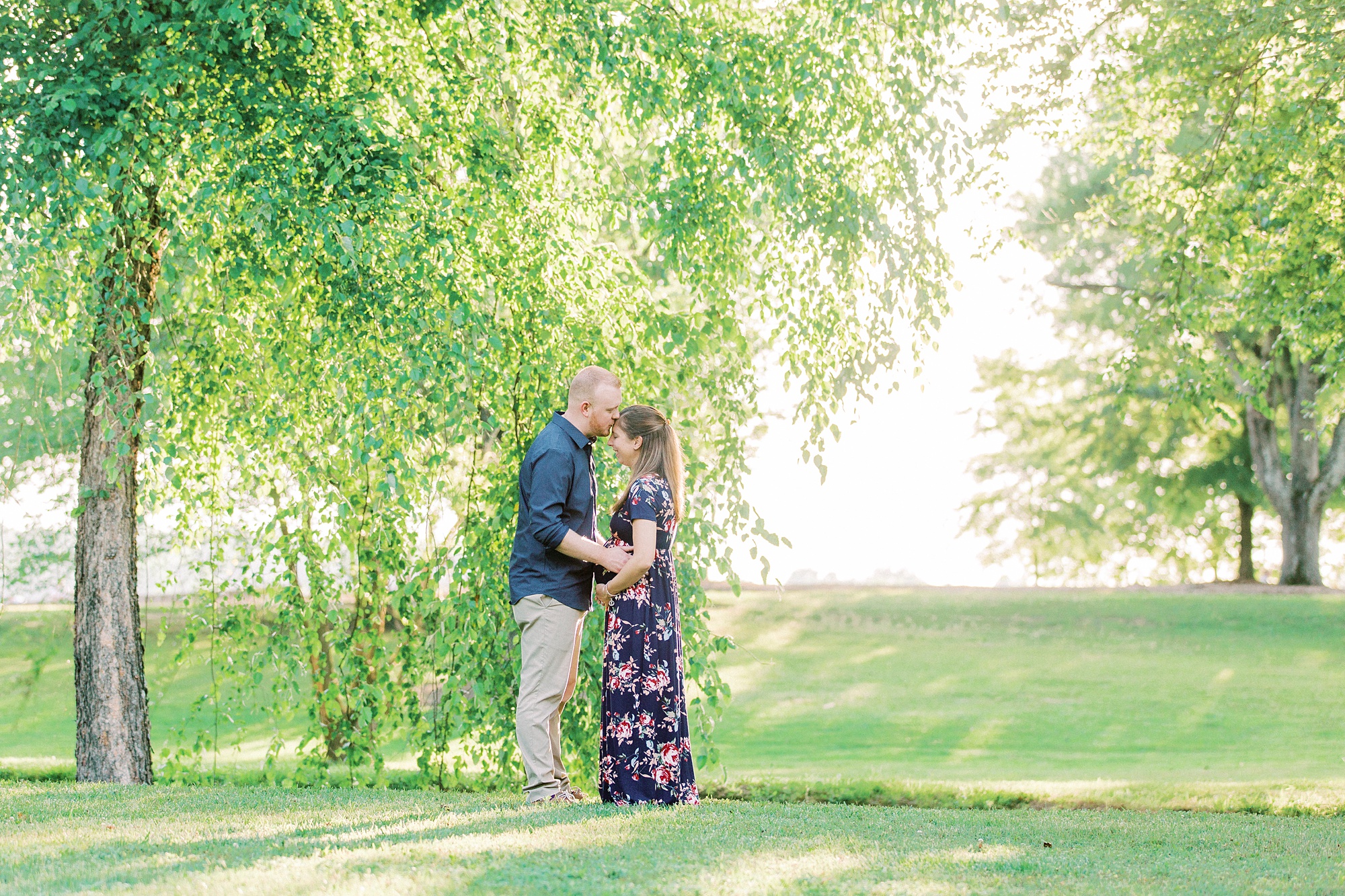 expecting parents pose under trees in Rankin Lake Park
