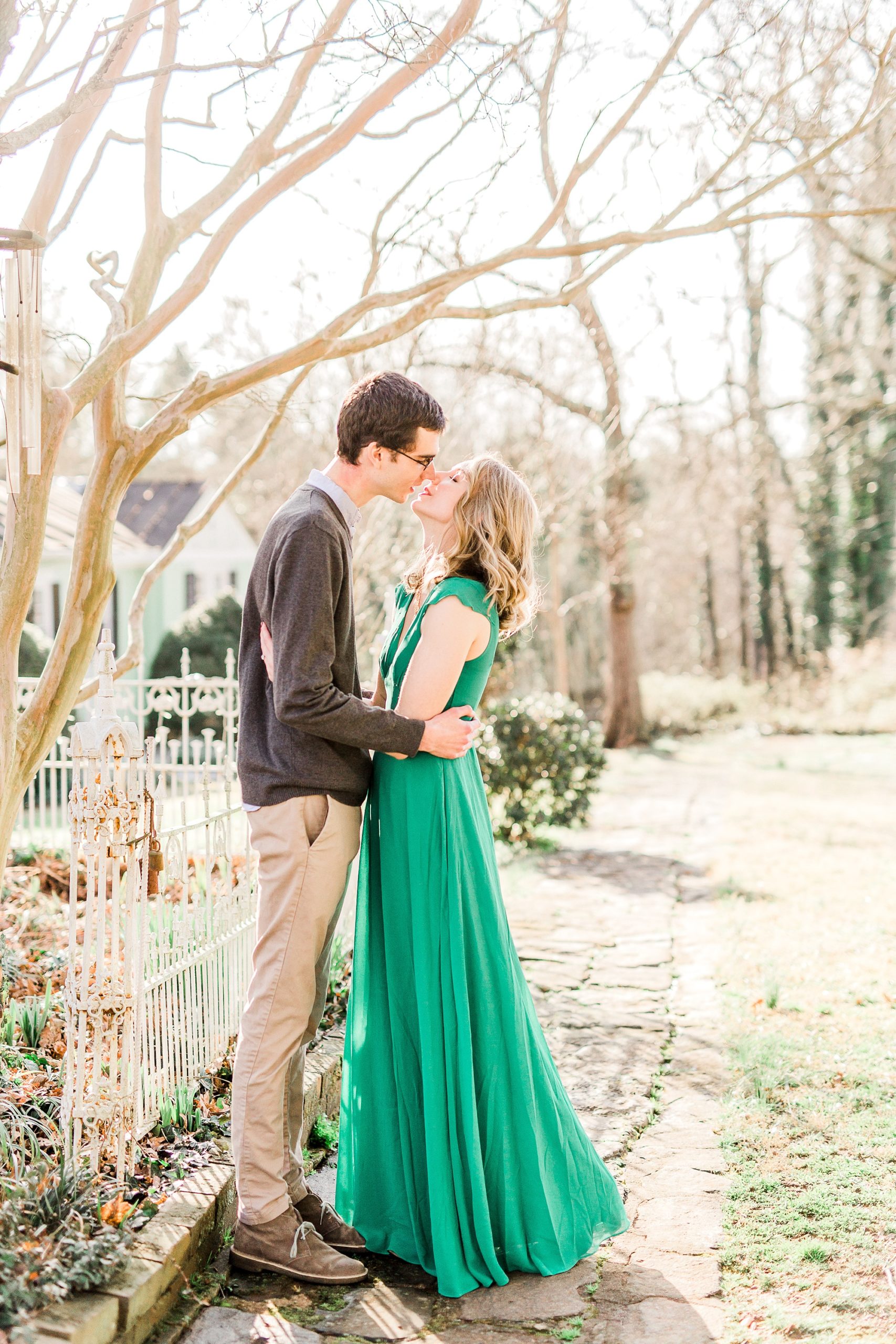 bride and groom stand by fence kissing during engagement photos