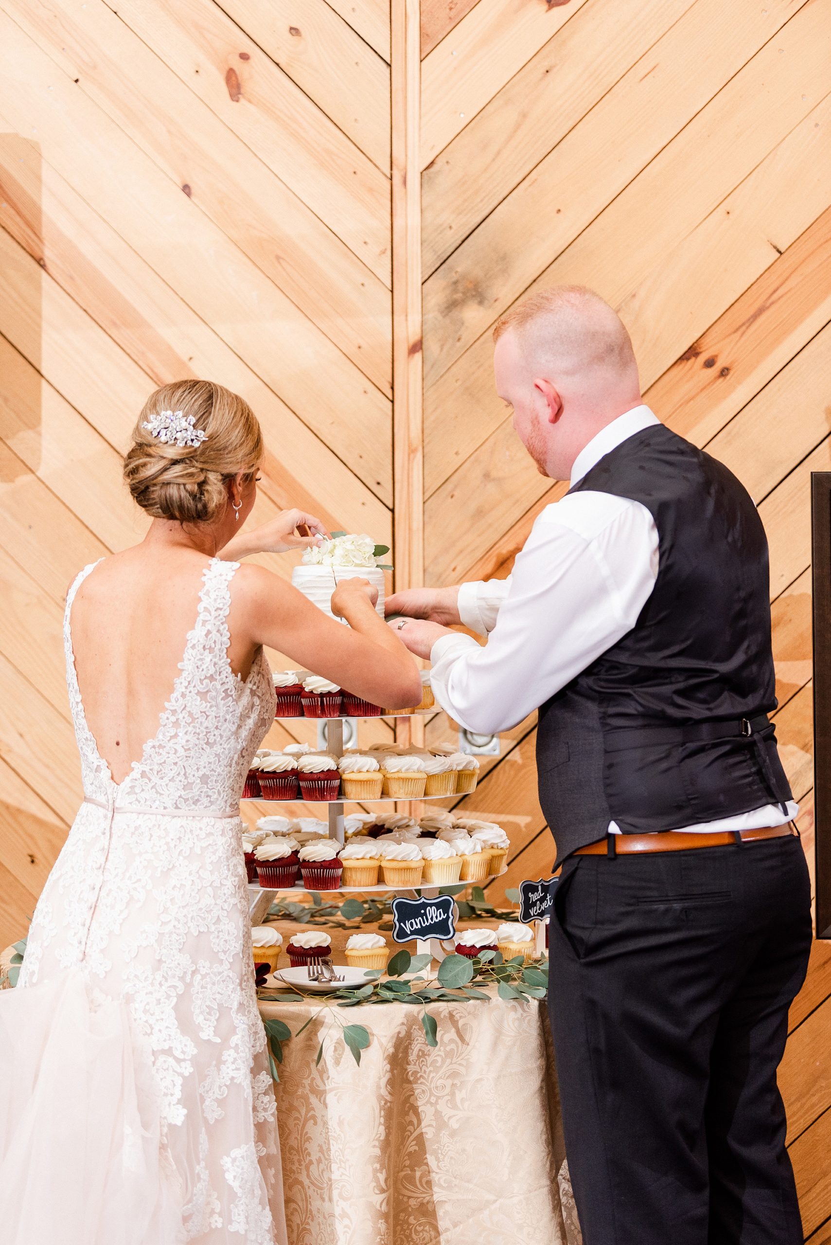 newlyweds cut wedding cake on top of cupcake tower at Charlotte NC wedding reception