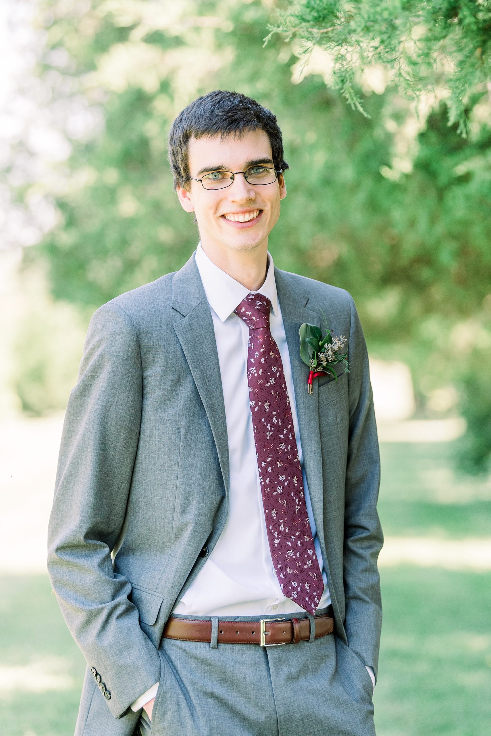 groom poses in grey suit with maroon tie
