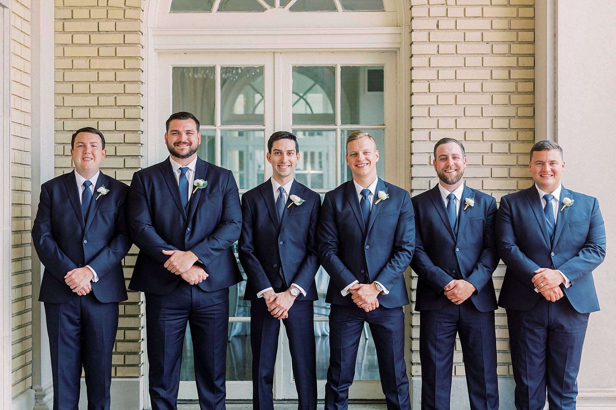 groom and groomsmen pose along brick wall at Separk Mansion