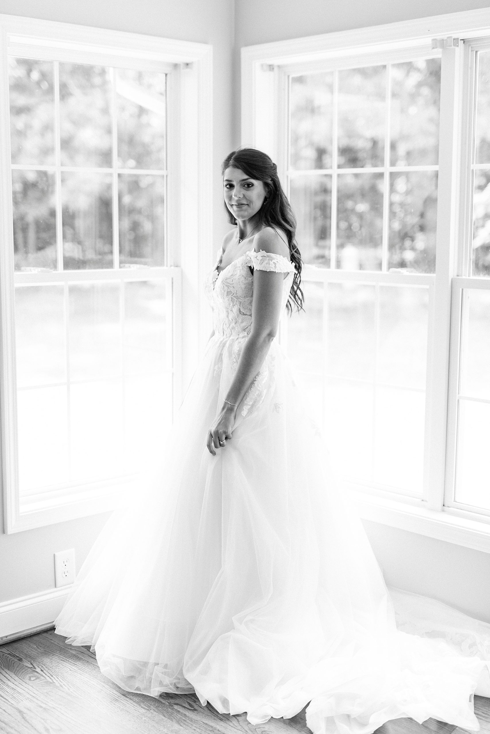 bride poses in window with wedding gown