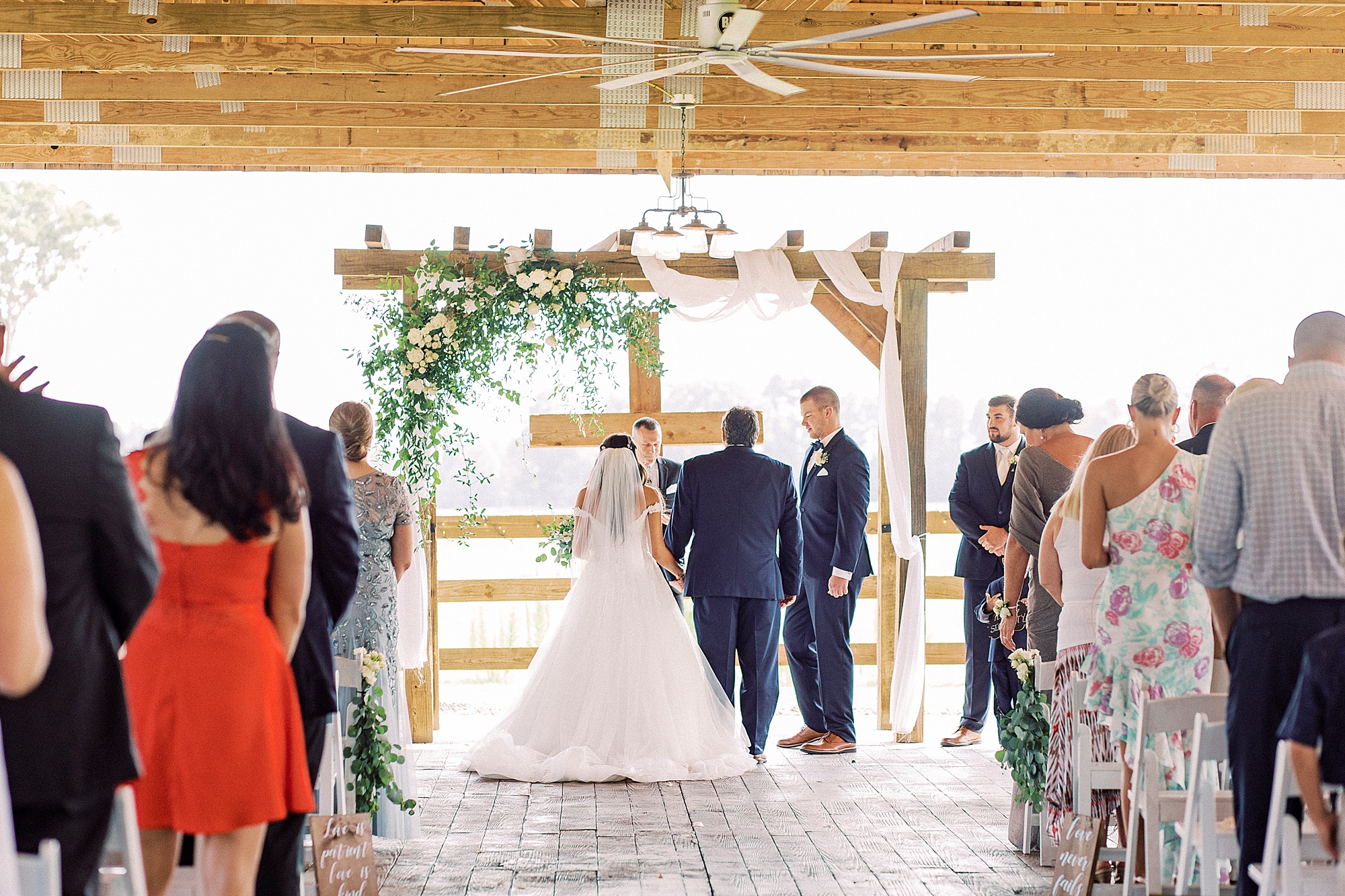 dad gives bride away during rustic wedding ceremony by wooden cross at The Farmstead