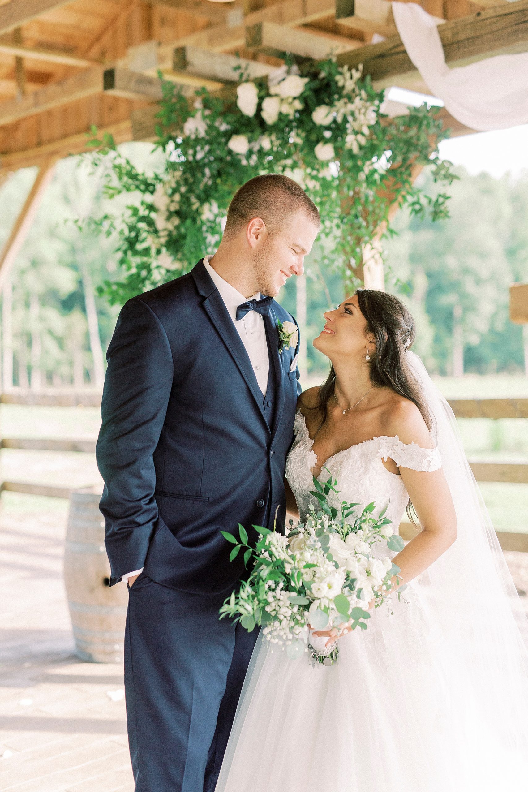 bride and groom look at each other by wooden cross at The Farmstead