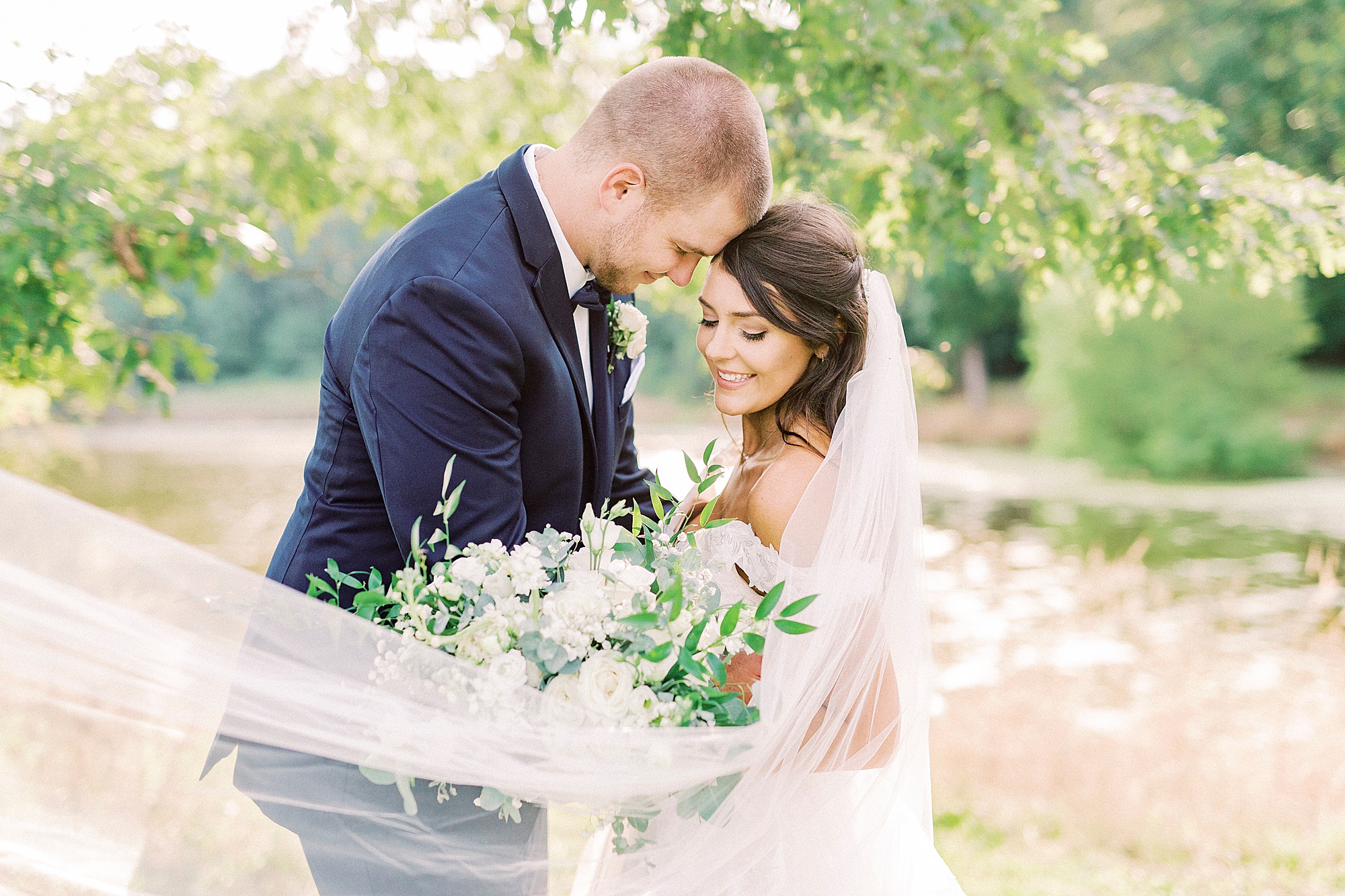 bride and groom hug with bride's veil around shoulders at The Farmstead