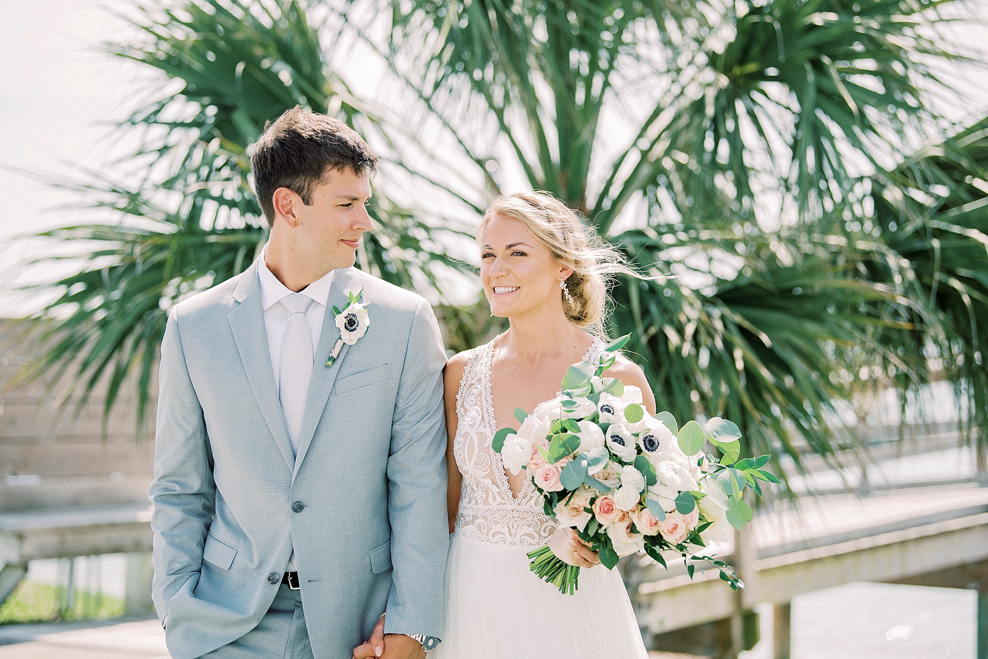 bride and groom walk by palm trees before Oceanic Restaurant wedding