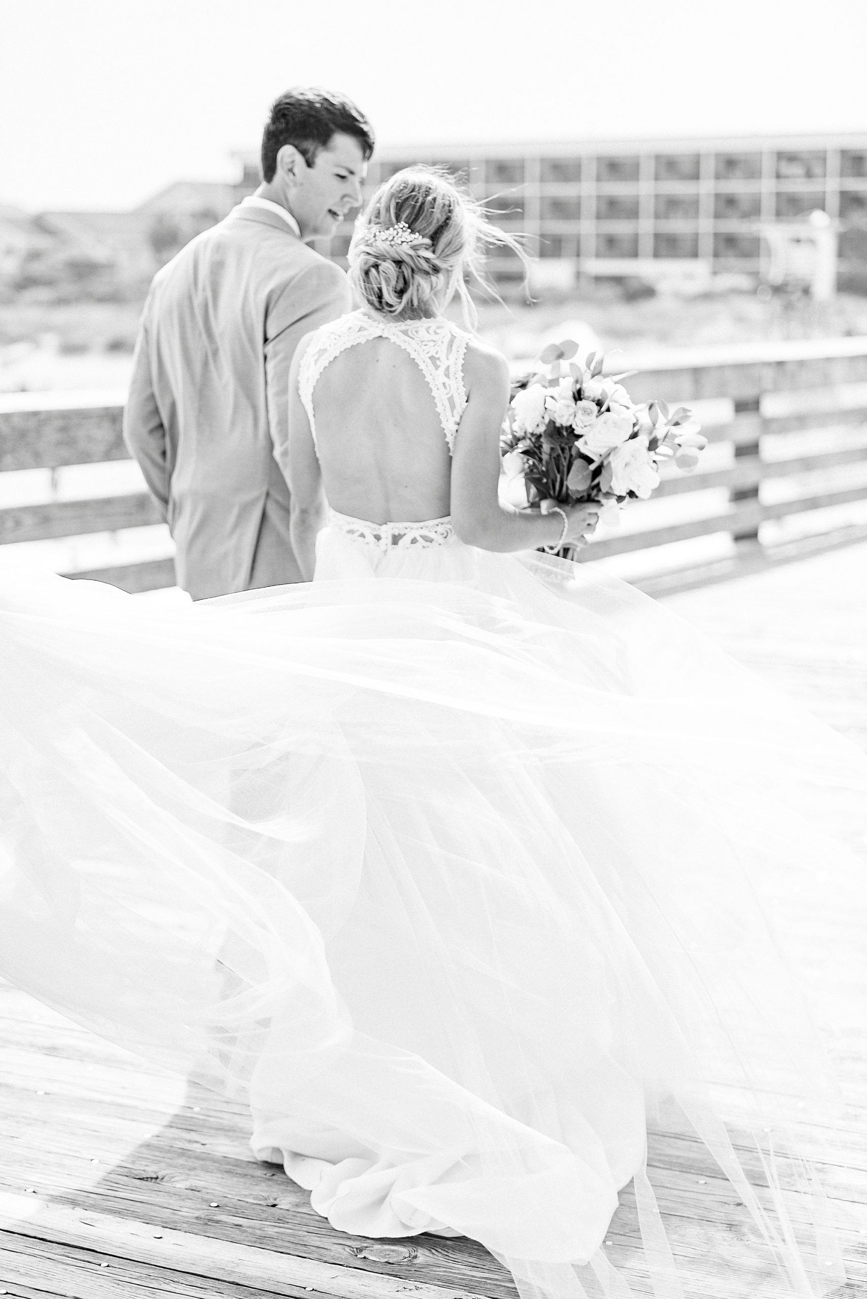 bride's dress blows in wind on pier after waterfront wedding ceremony in Wrightsville Beach