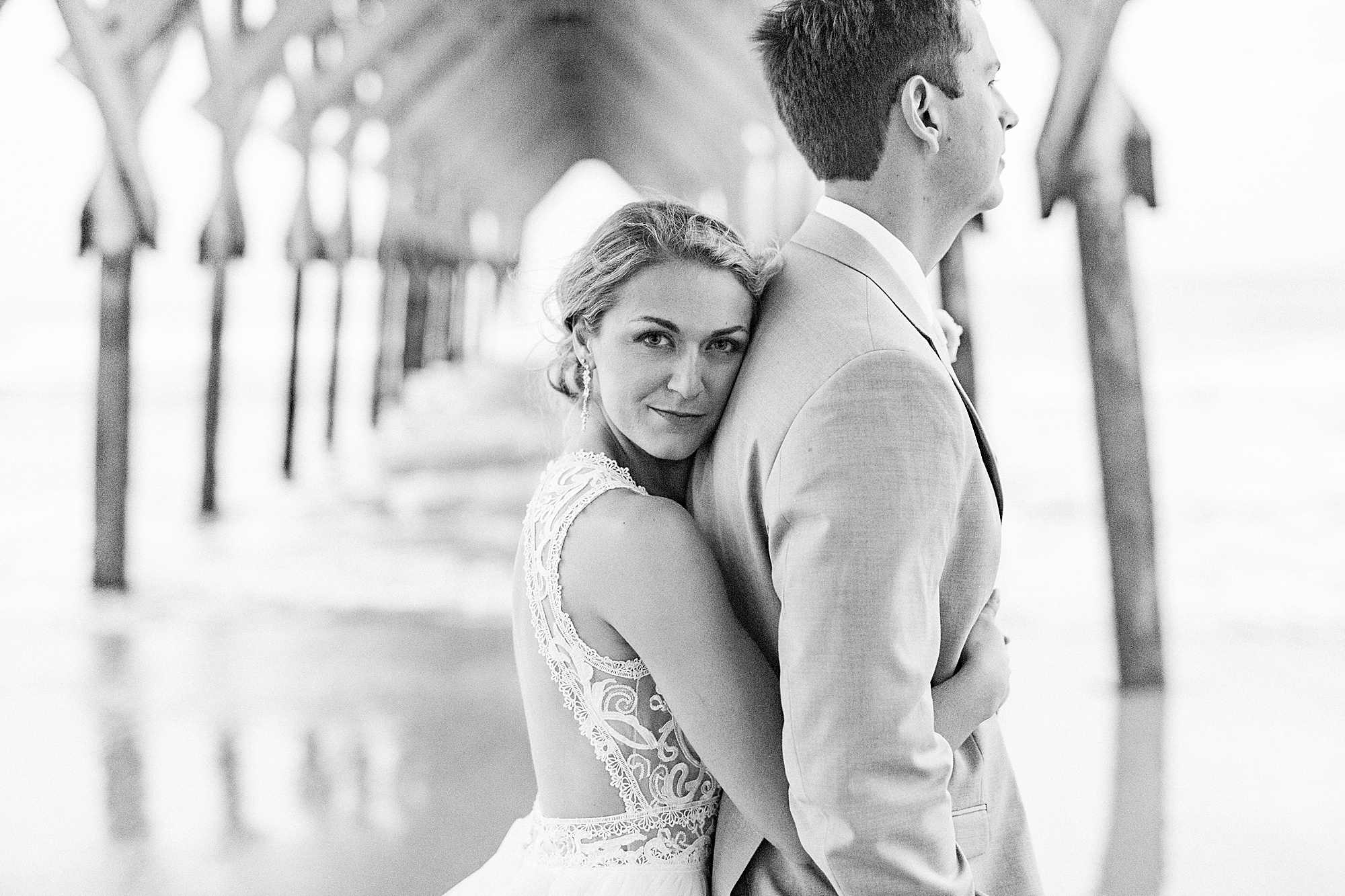 bride hugs groom from behind during NC wedding photos on beach