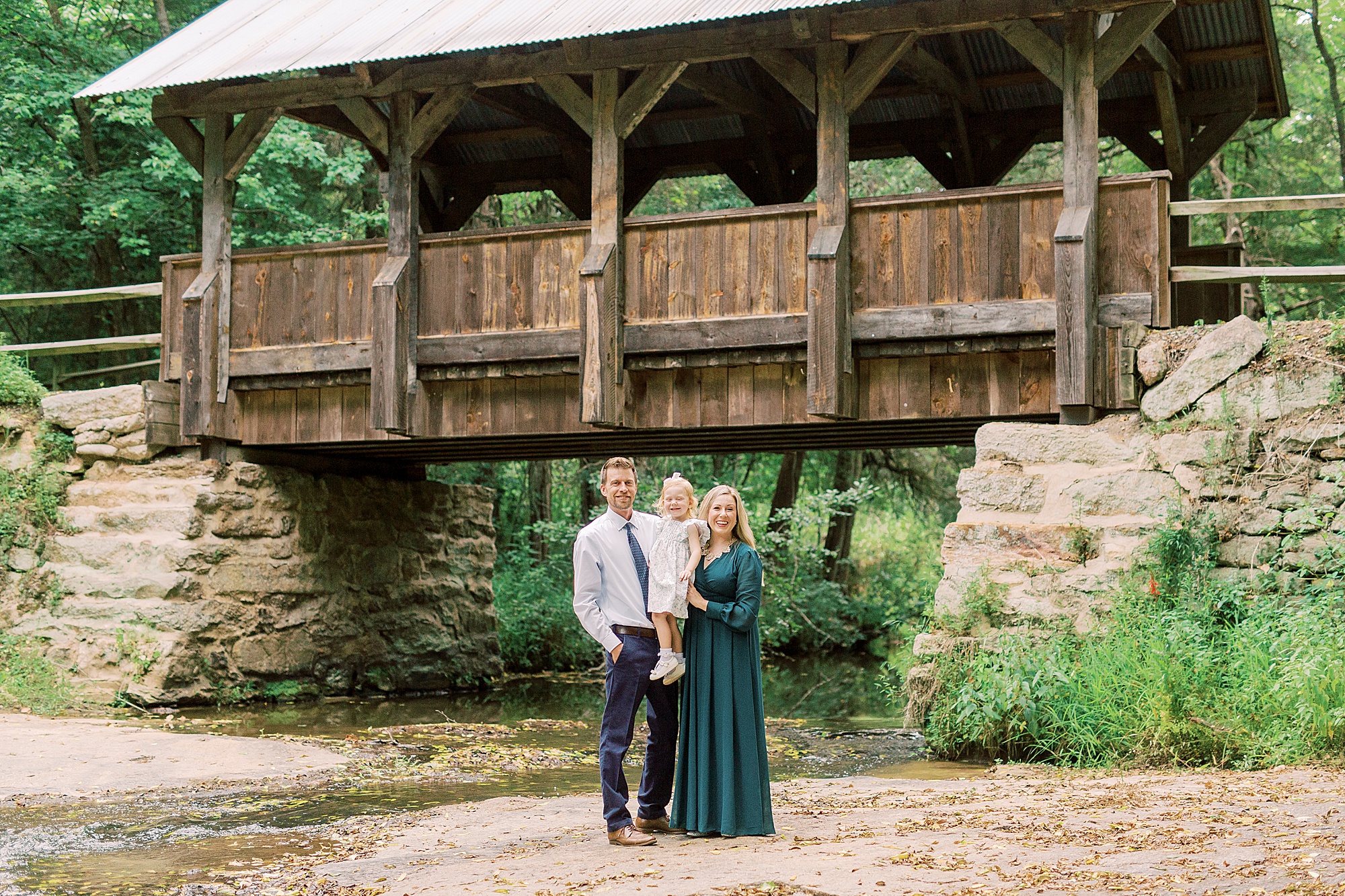family of three poses below covered bridge at Vesuvius Vineyards