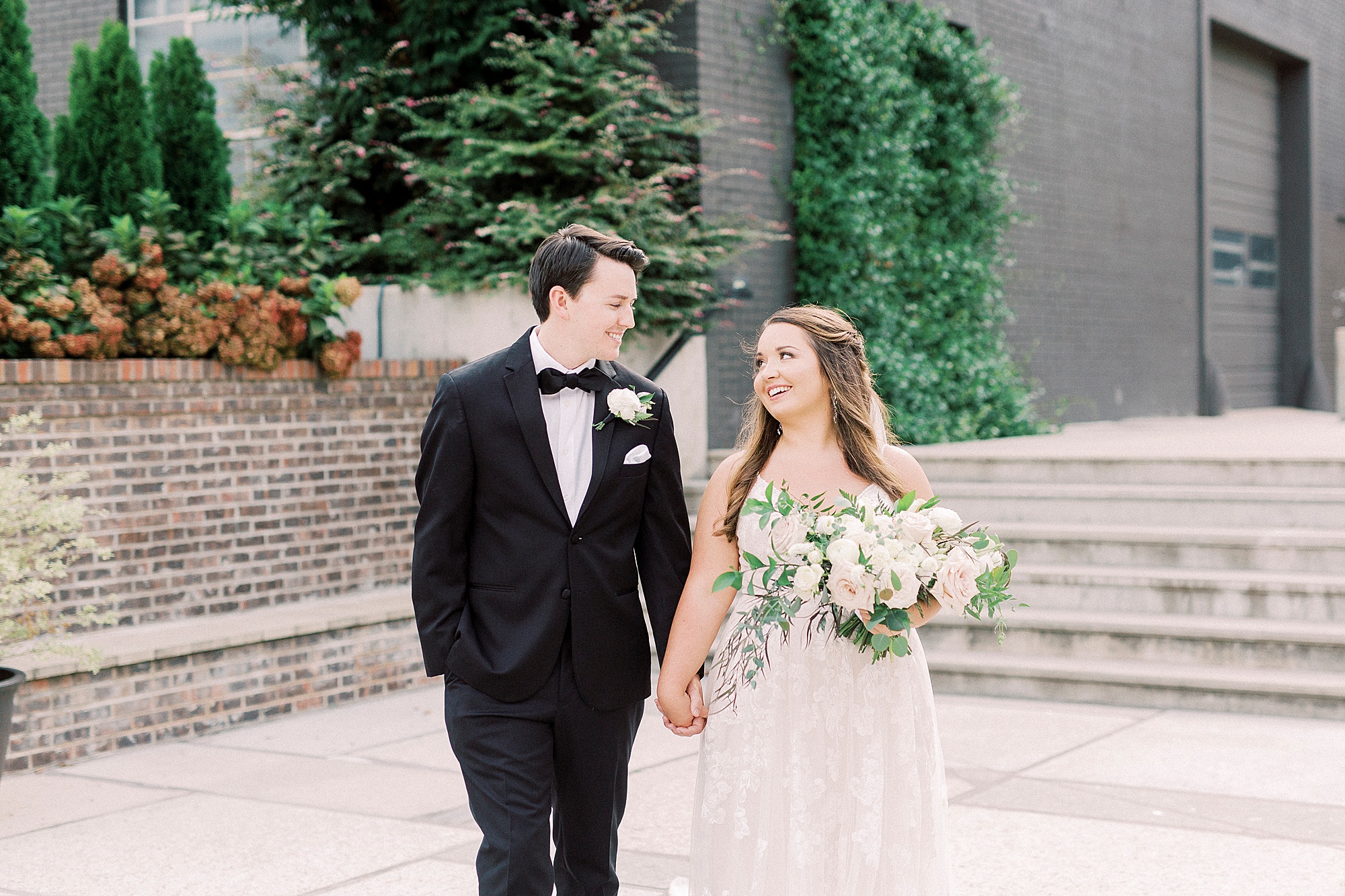 bride and groom hold hands walking outside Greensboro NC wedding venue