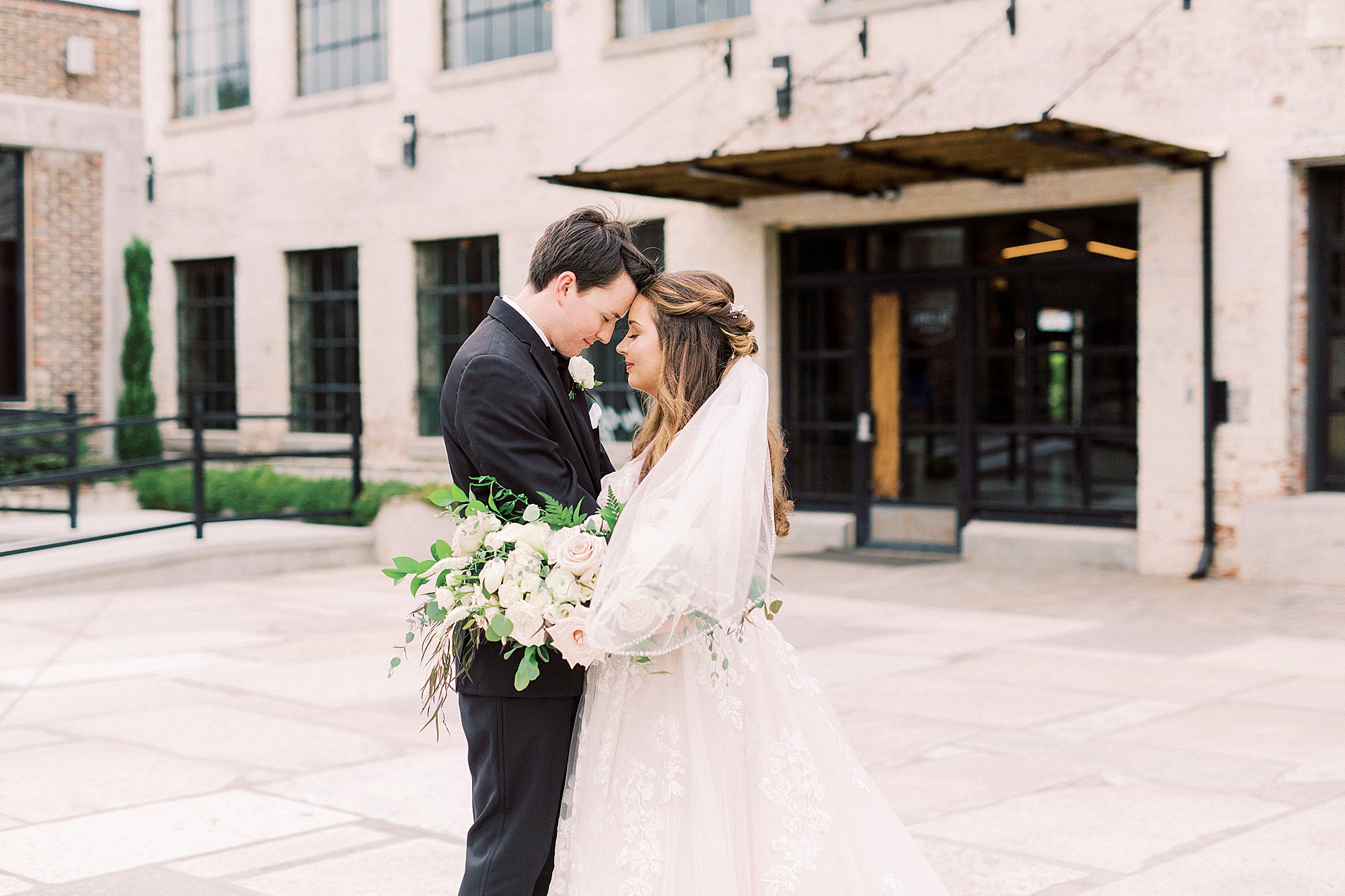 bride and groom pose with noses touching outside the Cadillac Service Garage