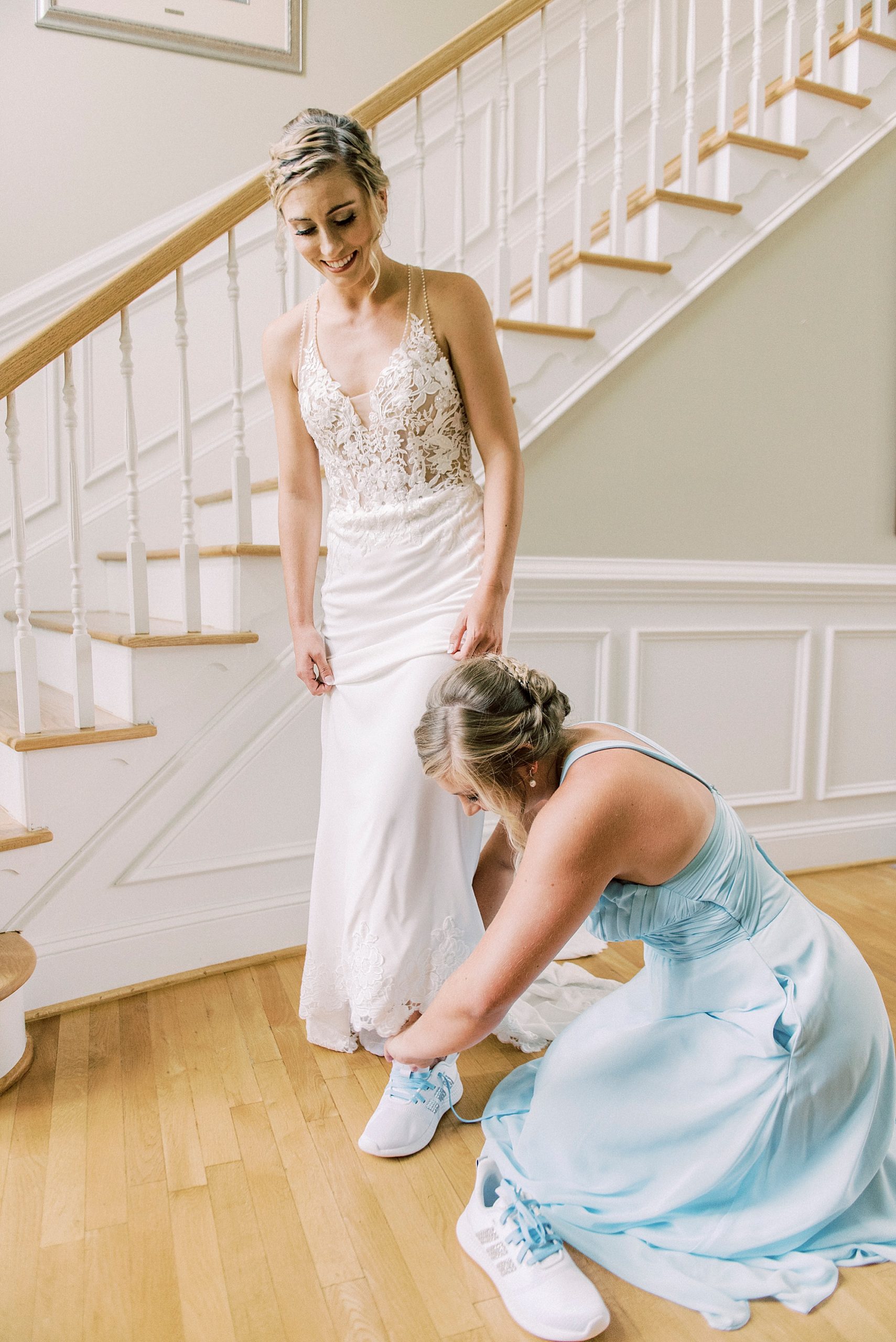 bridesmaid in blue dress helps bride with dress