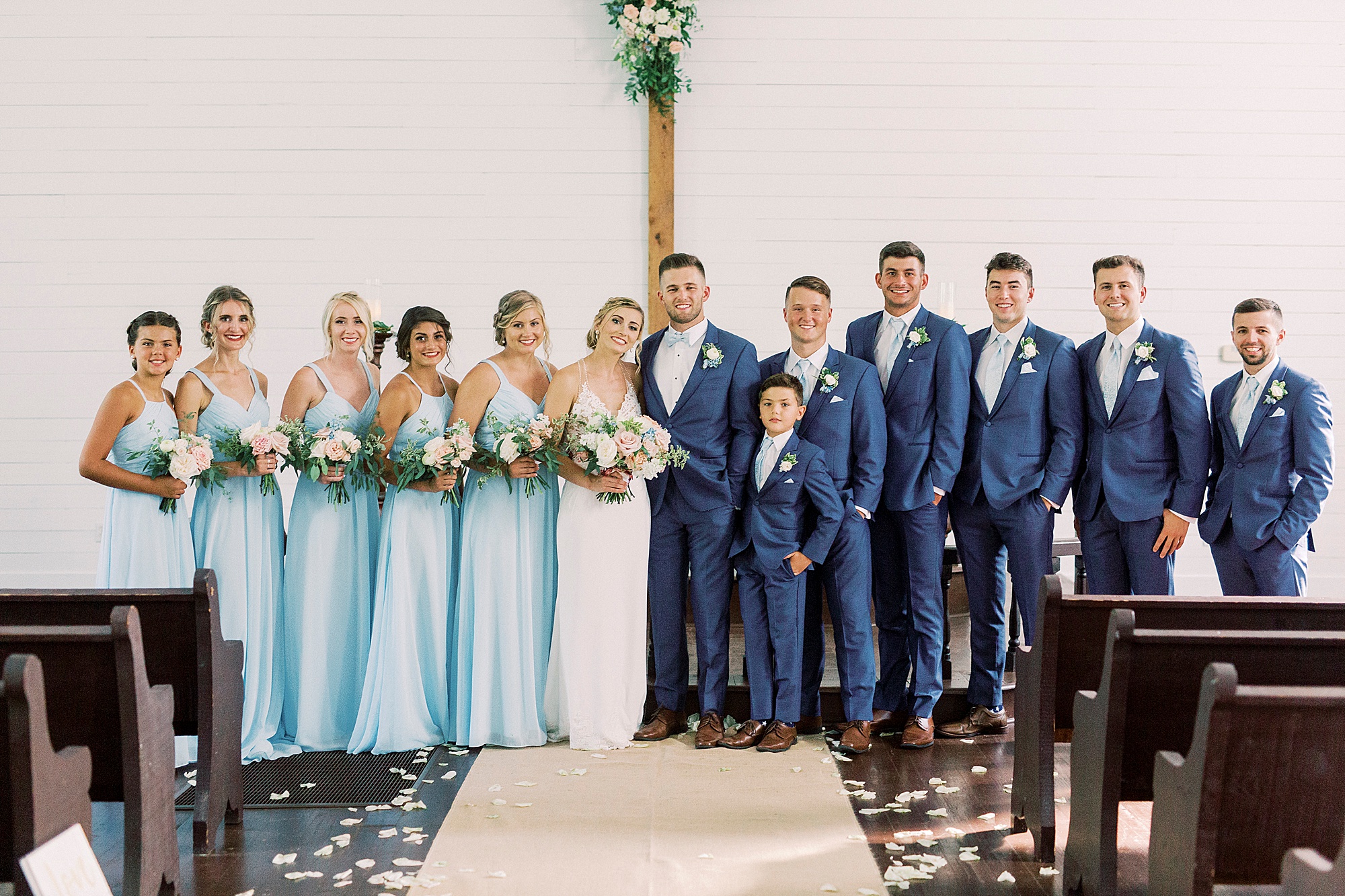bride and groom pose with wedding party in white church