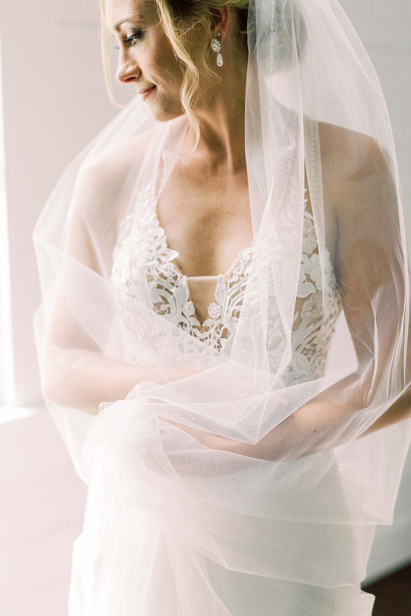 bride holds veil during portraits by church windows