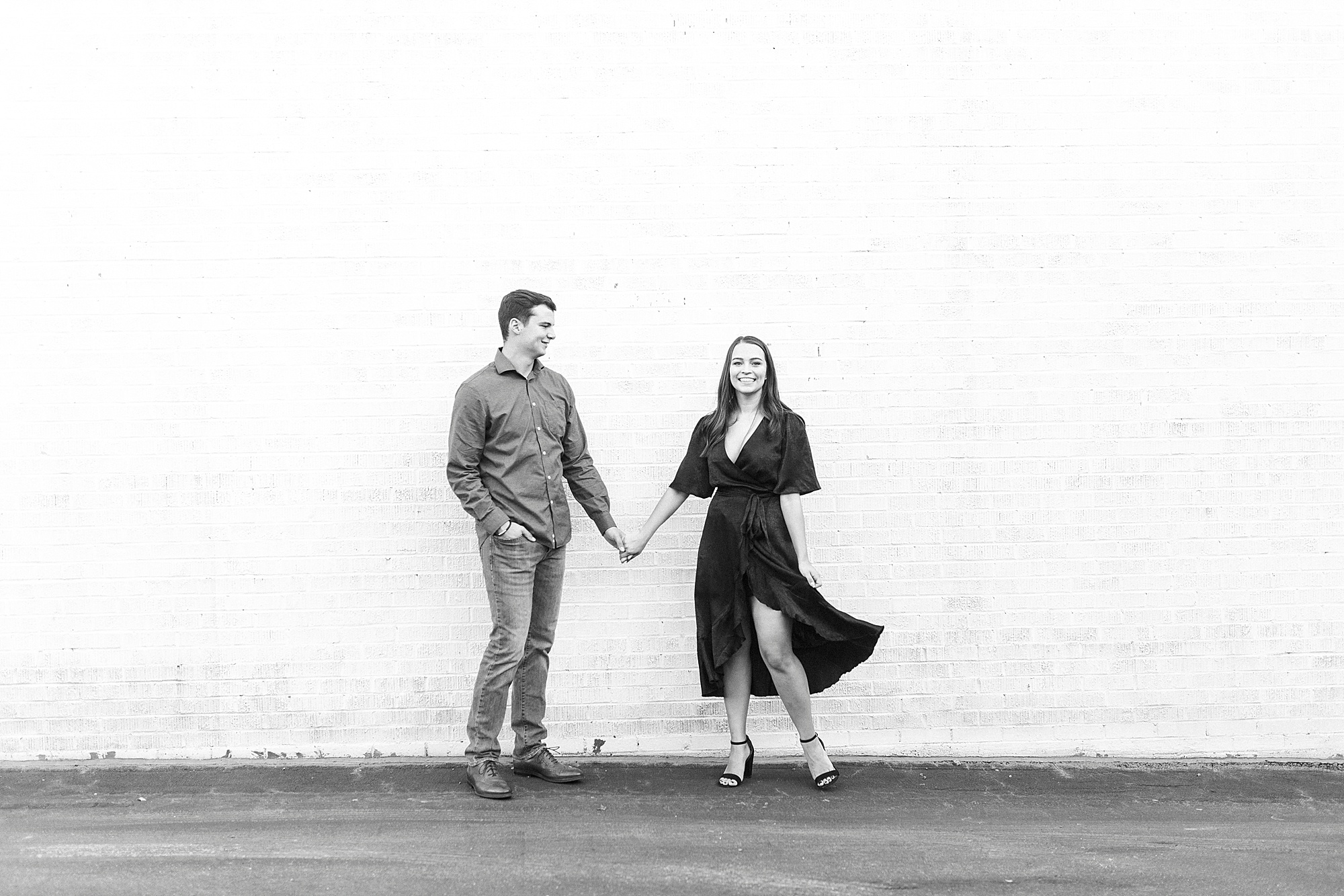 couple holds hands by white wall in Downtown Concord