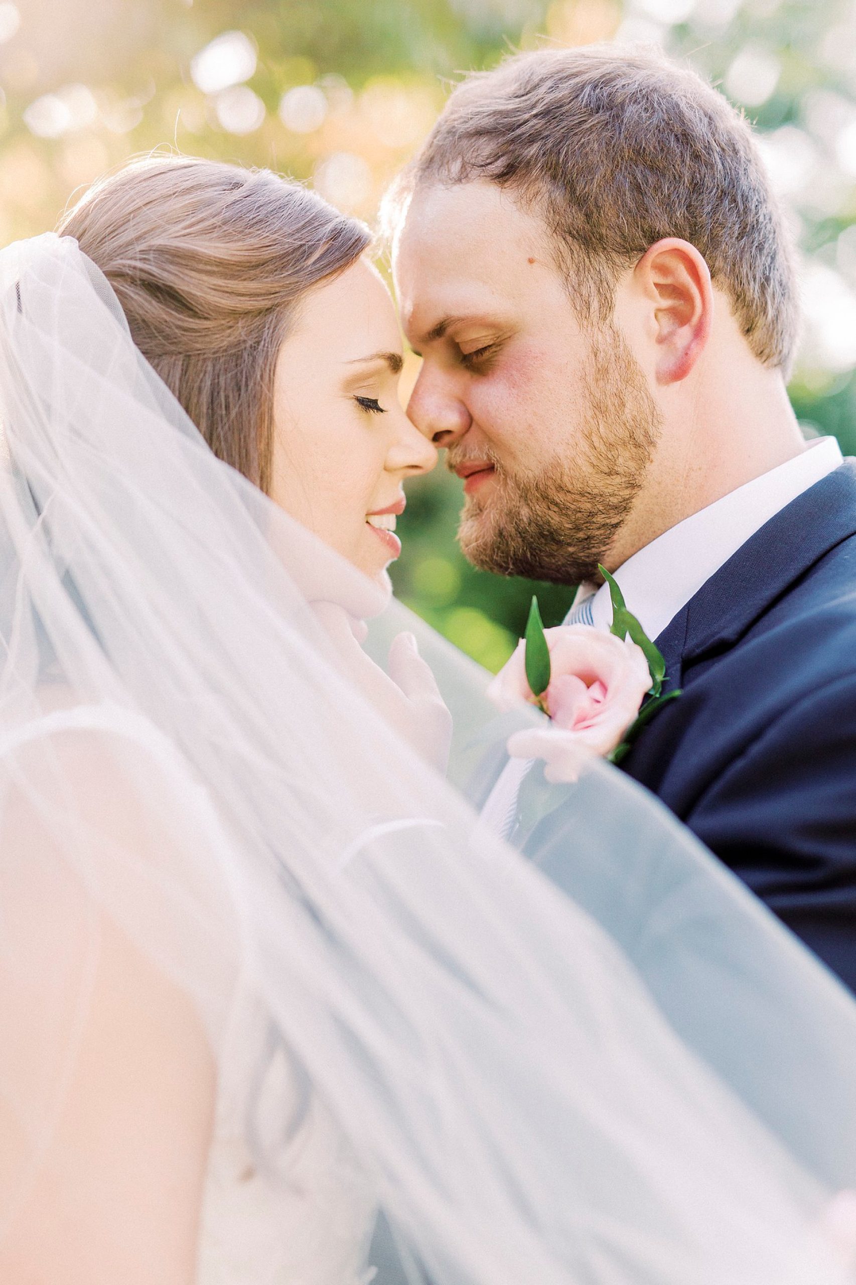 bride and groom stand nose to nose under bride's veil