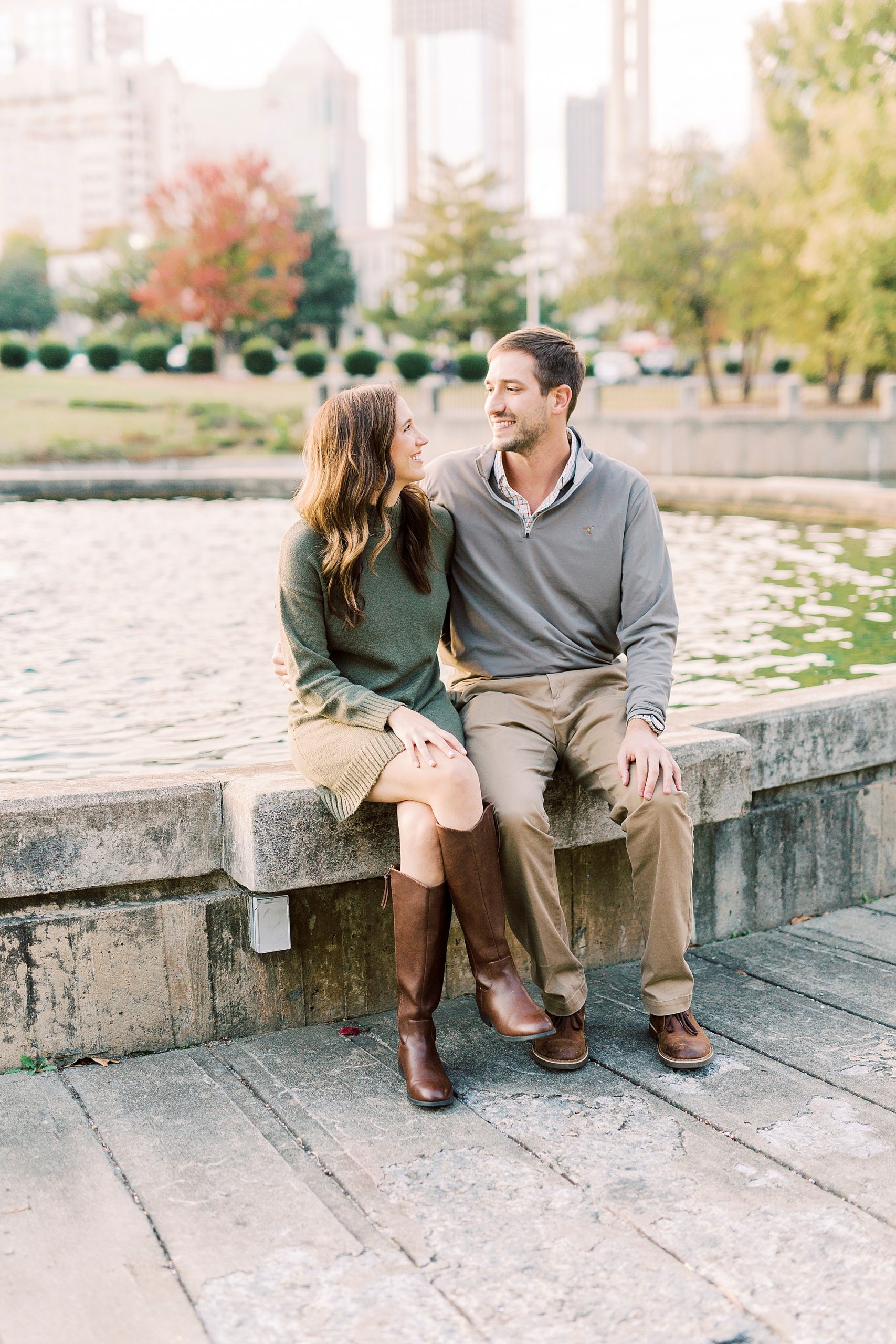 engaged couple laughs sitting on fountain in Charlotte NC