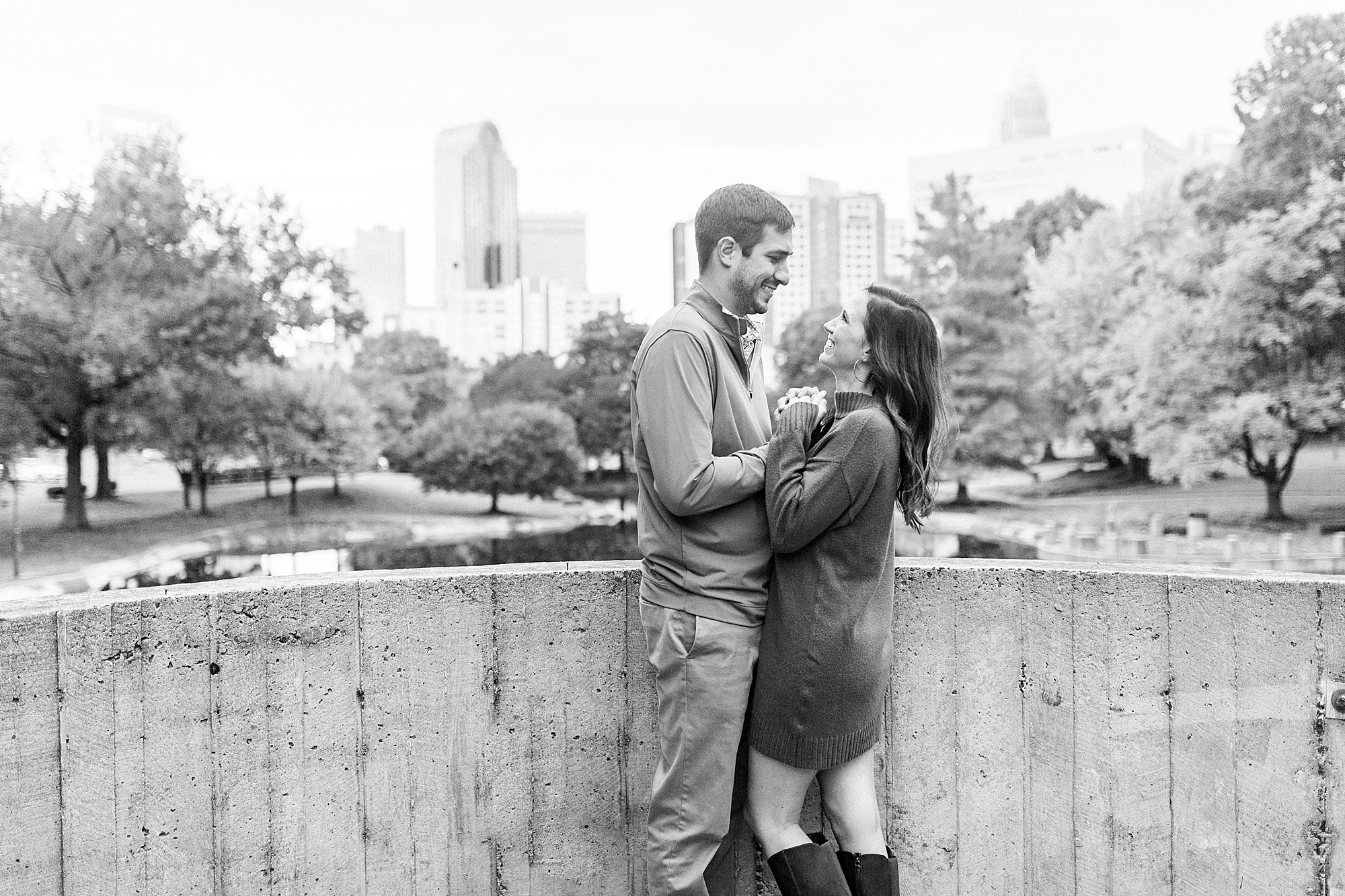 engaged couple smiles with Charlotte skyline behind them