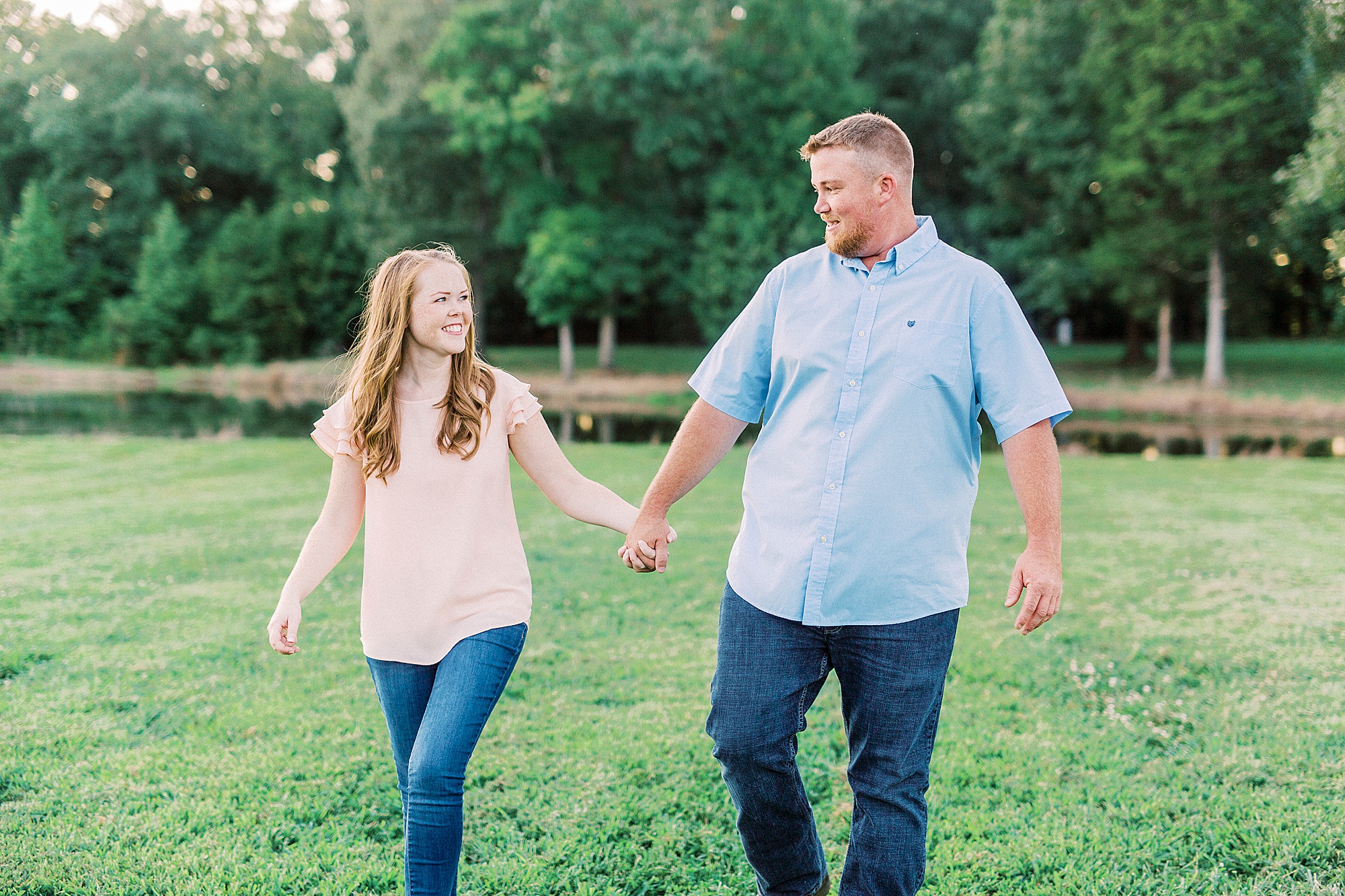 couple holds hands walking through field at Sunset Farms