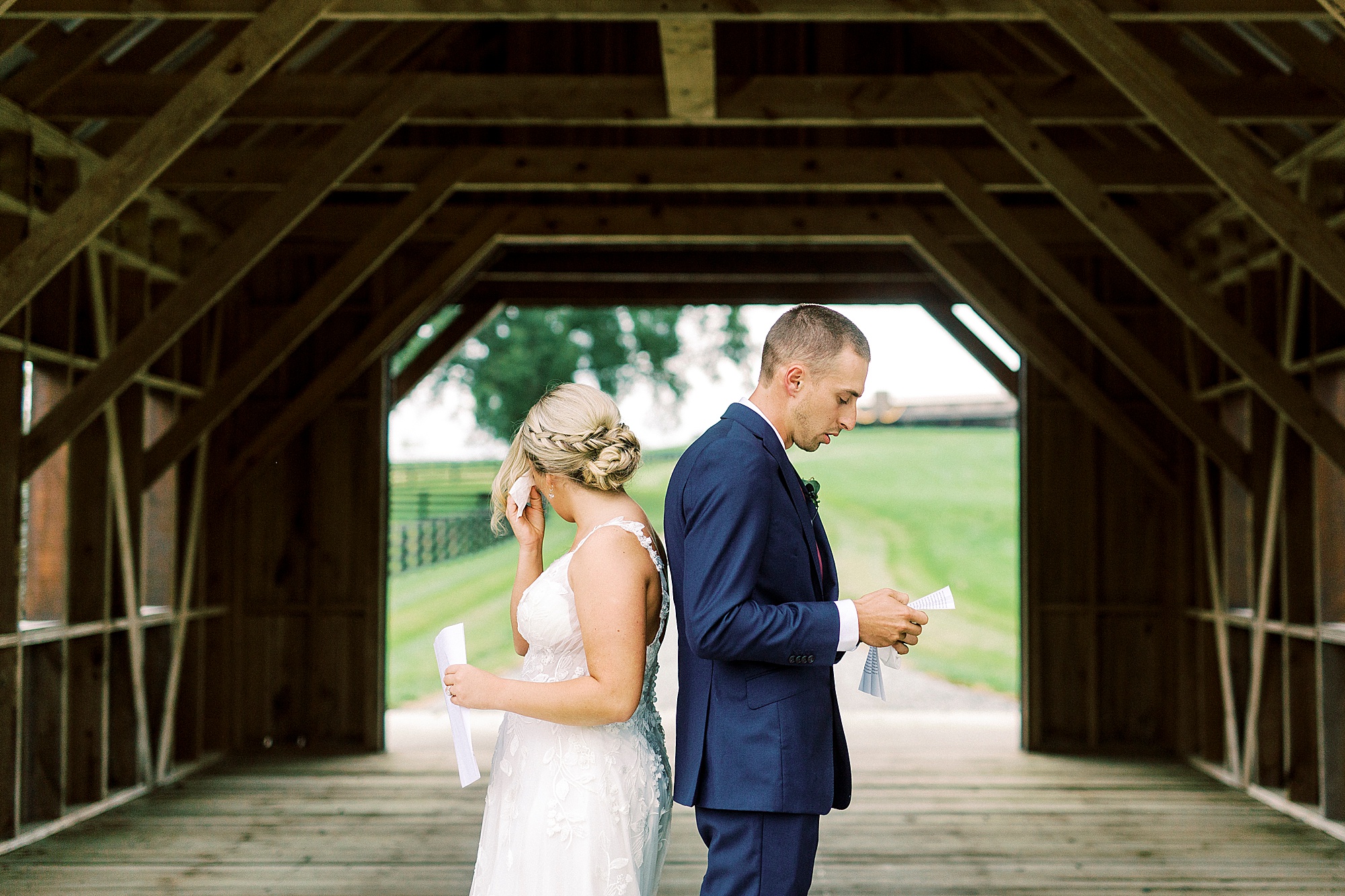 bride and groom stand back to back reading vows