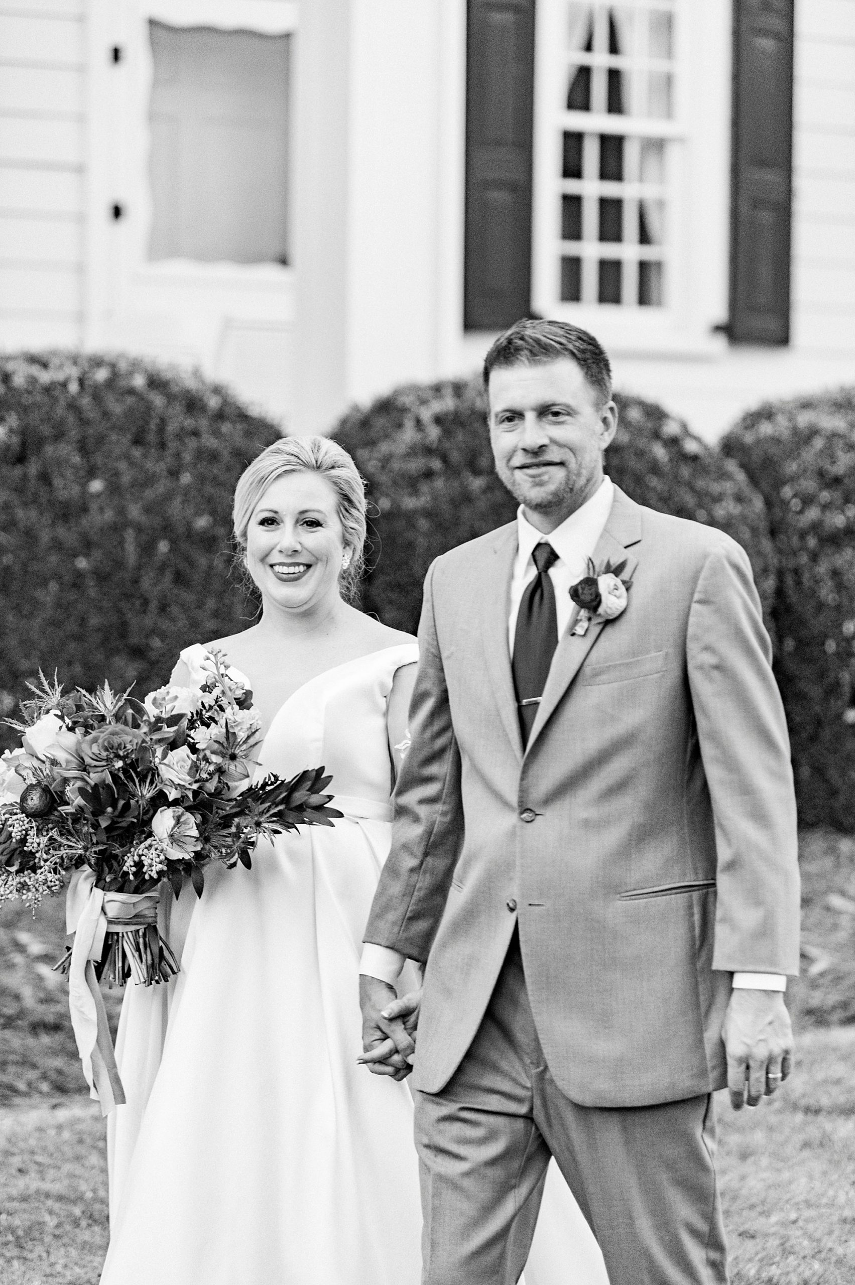 newlyweds hold hands walking by manor house at Vesuvius Vineyards
