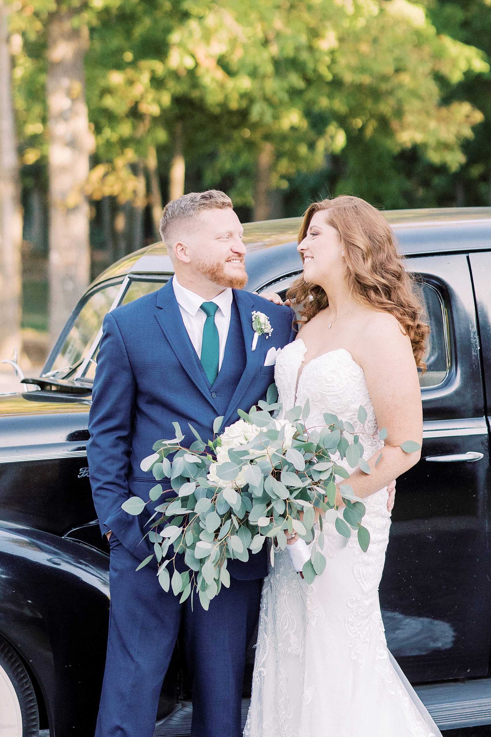 newlyweds smile together outside classic car
