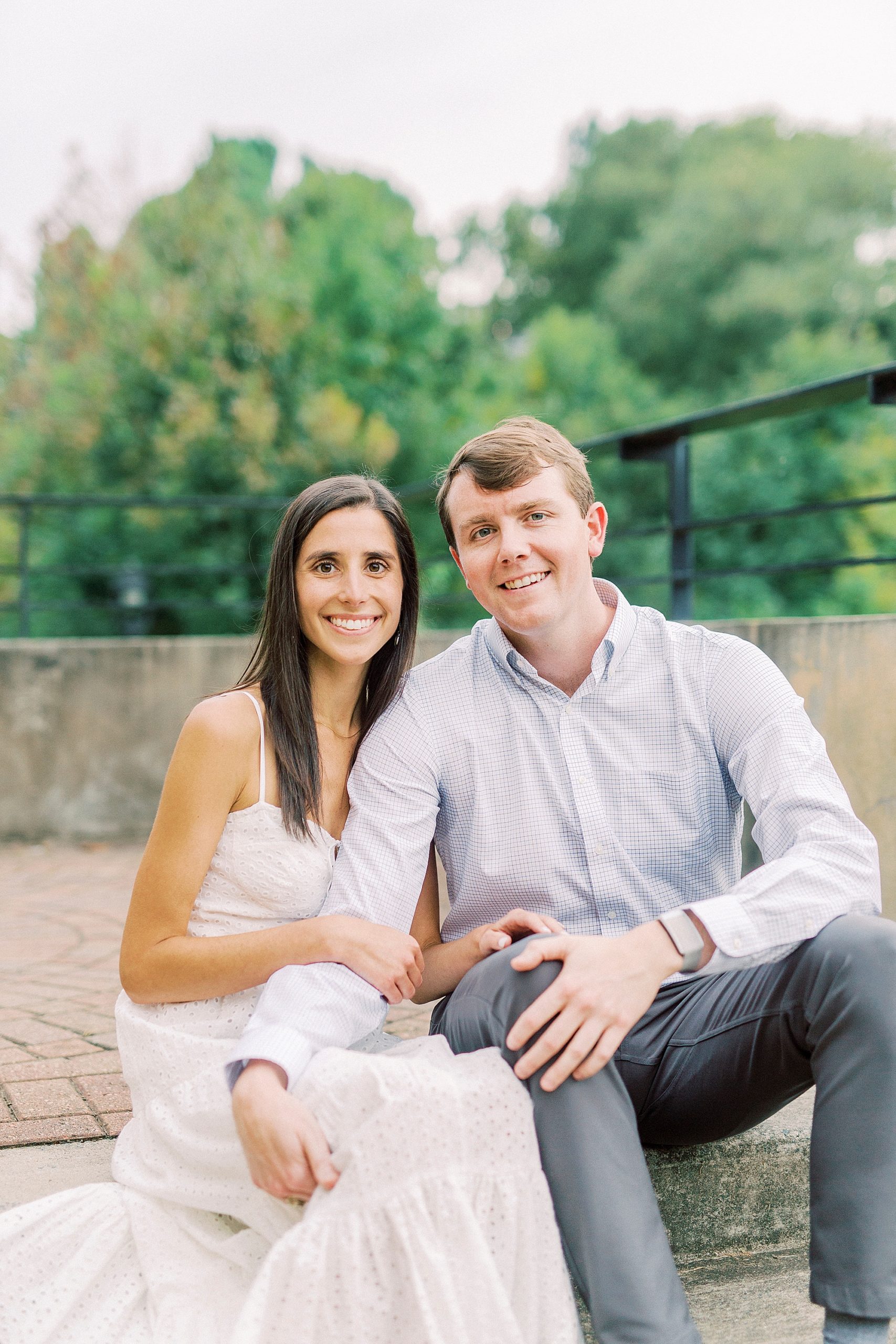 engaged couple sits on stone steps in Midtown Park during engagement session