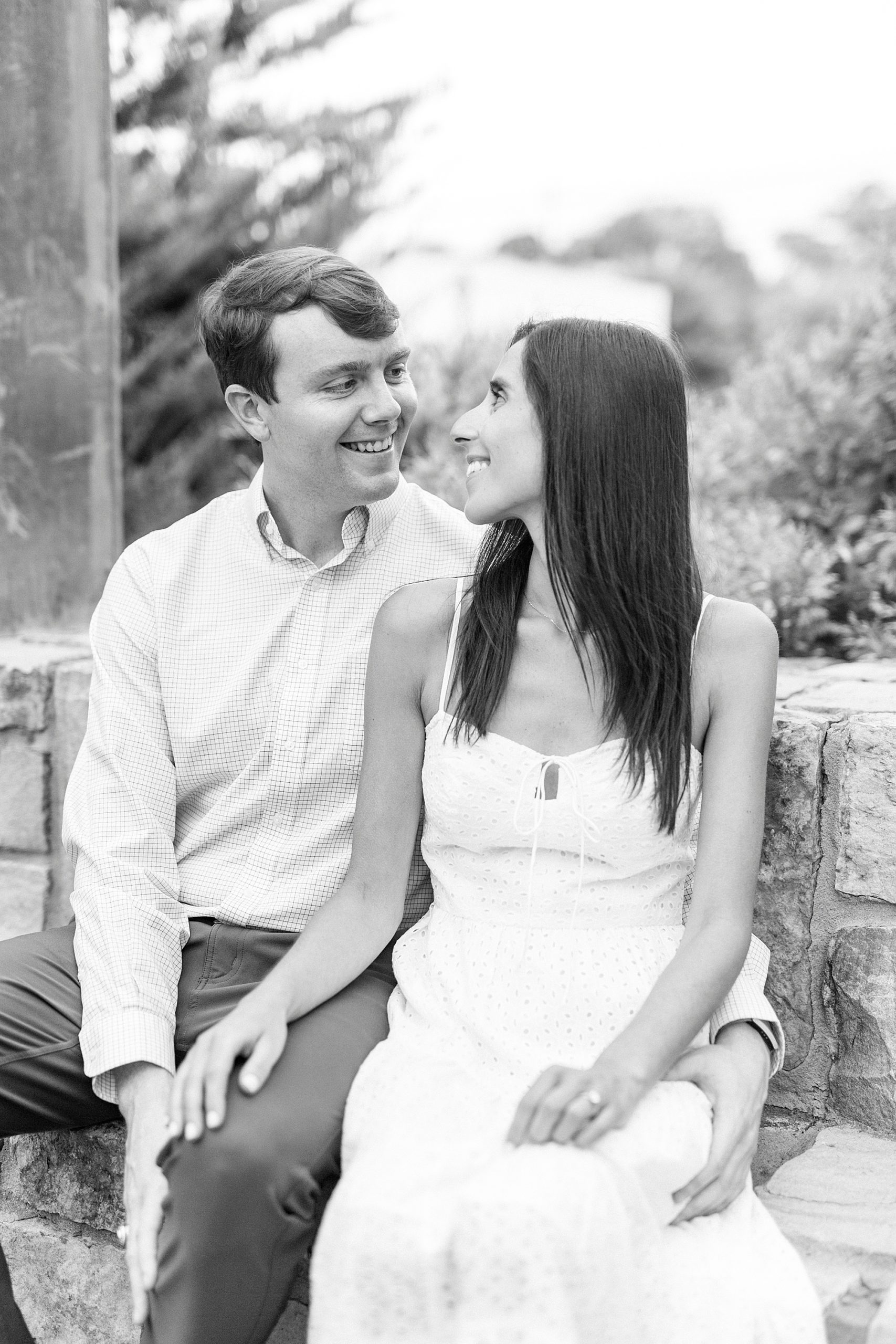 engaged couple sits on stone bench smiling together