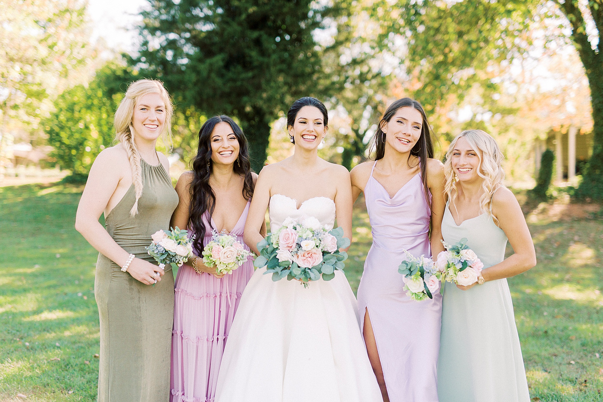 bride poses with bridesmaids in mismatched pastel gowns
