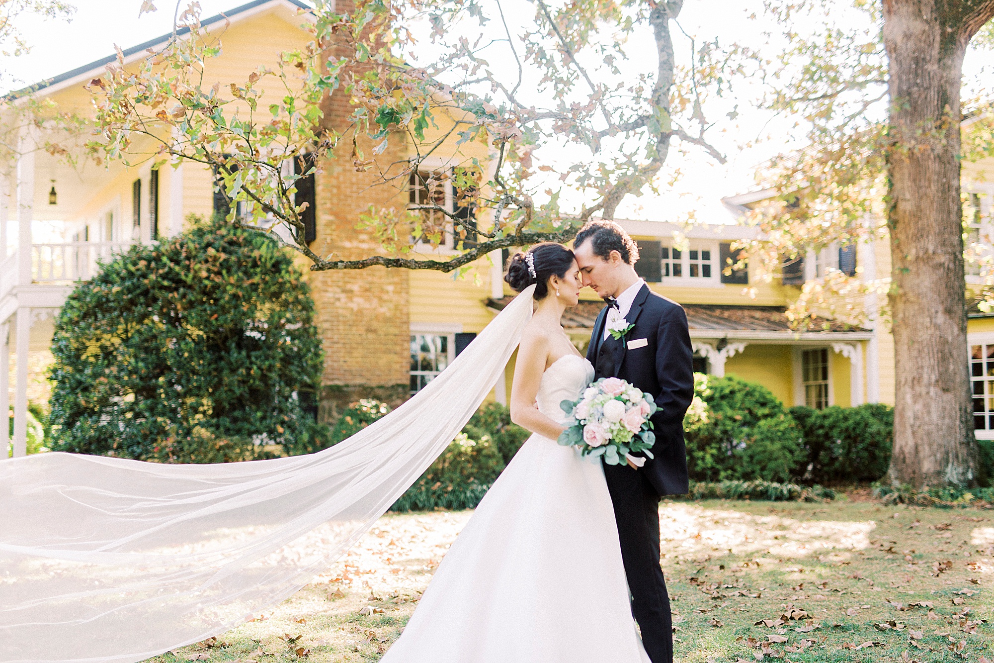 bride and groom stand with foreheads touching and veil behind them