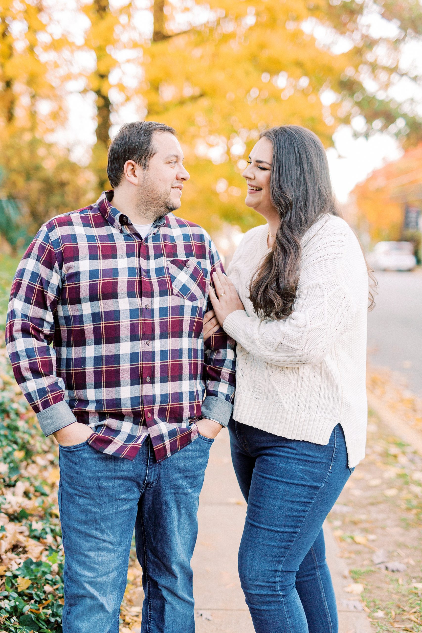 bride and groom stand with yellow trees behind them on sidewalk in the fall