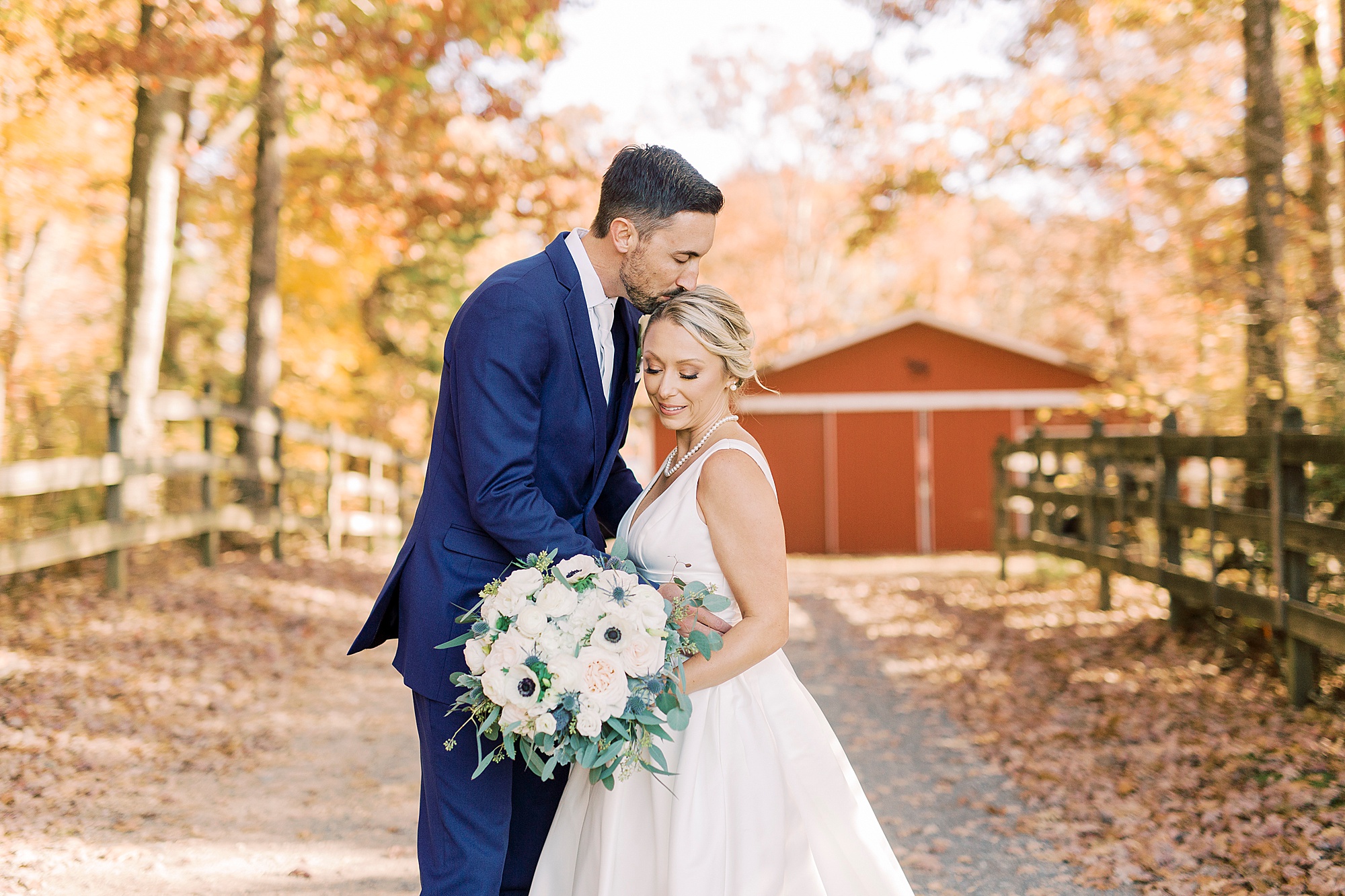 groom kisses bride's forehead during portraits by red barn at the Farm at Brusharbor