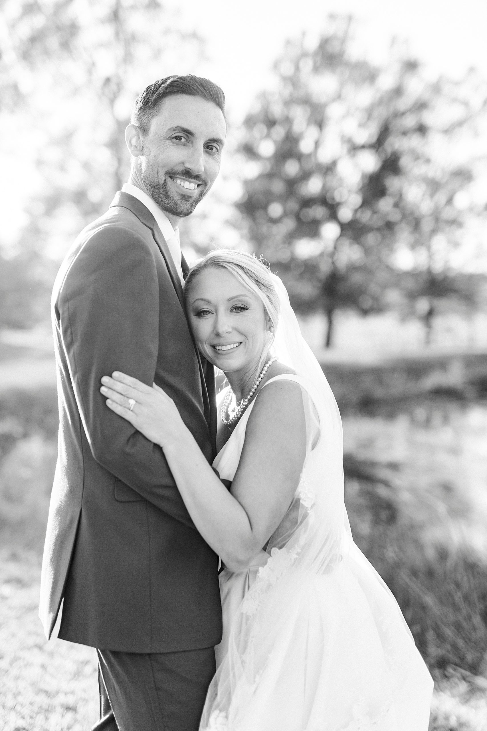 bride leans against groom's chest along waterfront at the Farm at Brusharbor