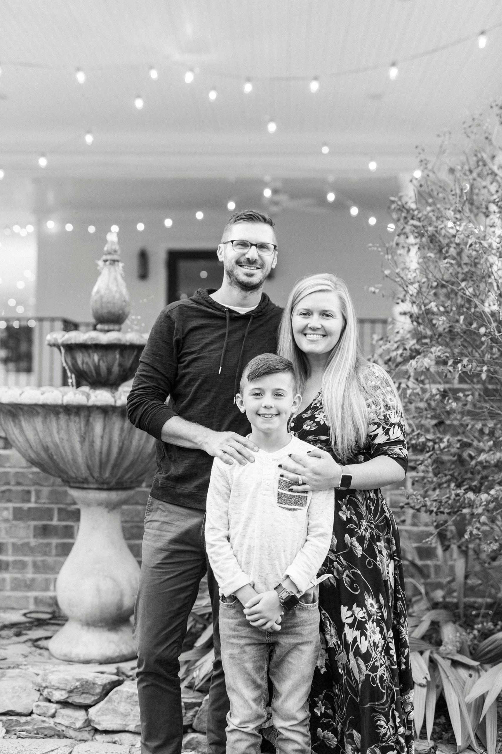 family of three poses outside Ritchie Hill with string lights