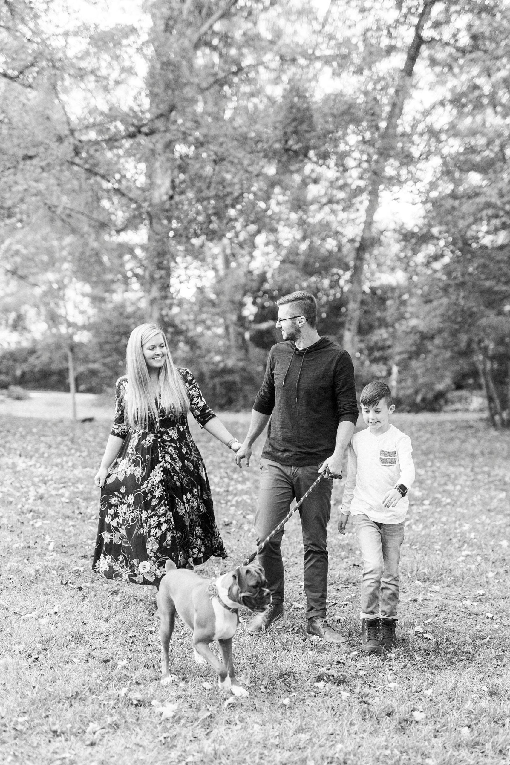 couple holds hands walking with son and dog
