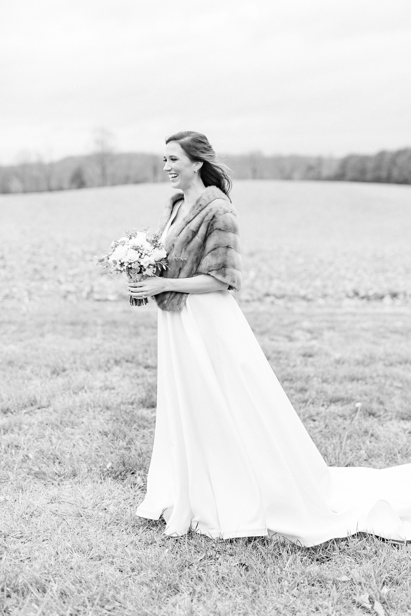 bride stands in field with fur wrap and wedding bouquet
